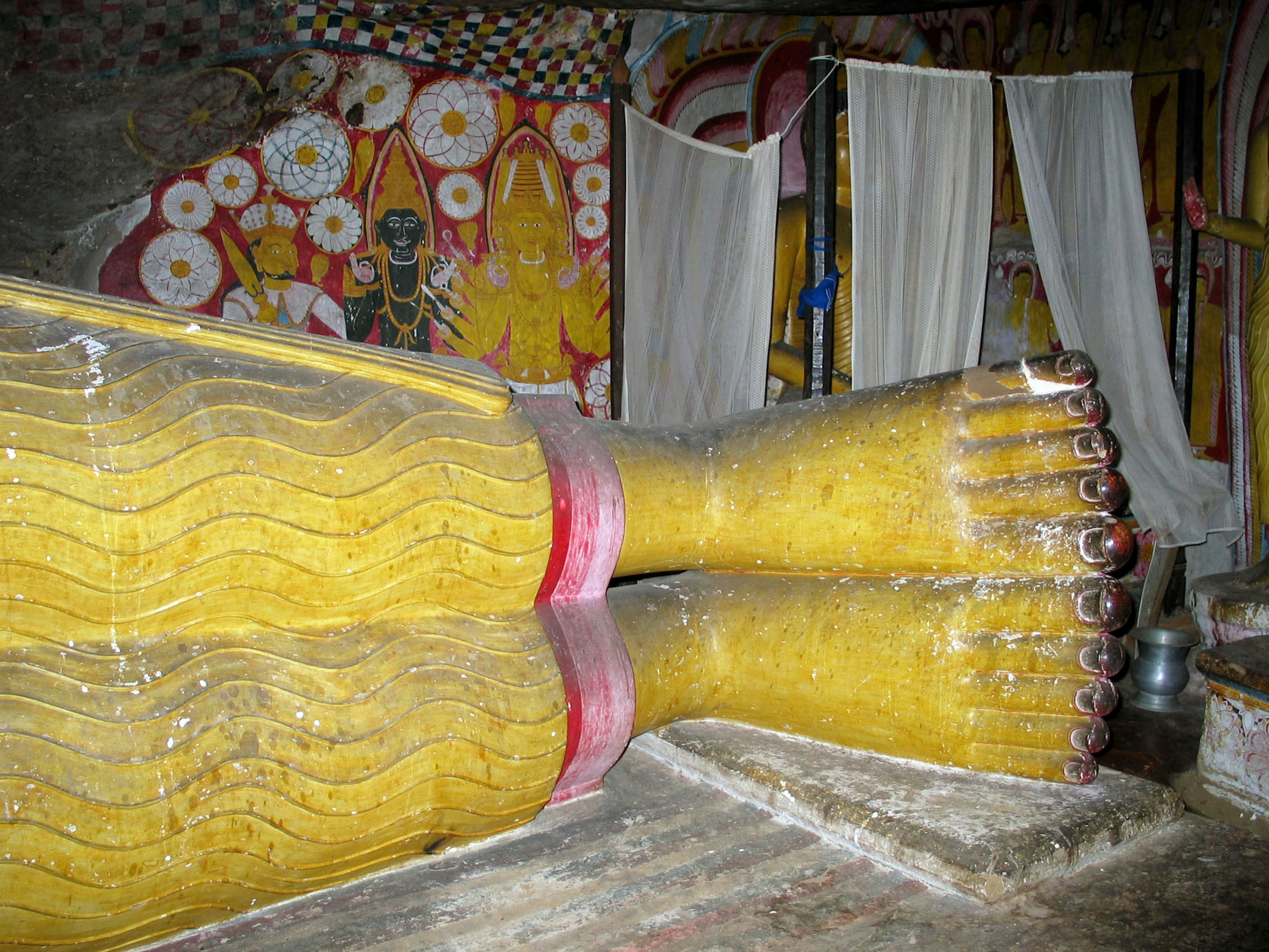 Vista dei grandi piedi di una statua di Buddha con affreschi colorati sullo sfondo