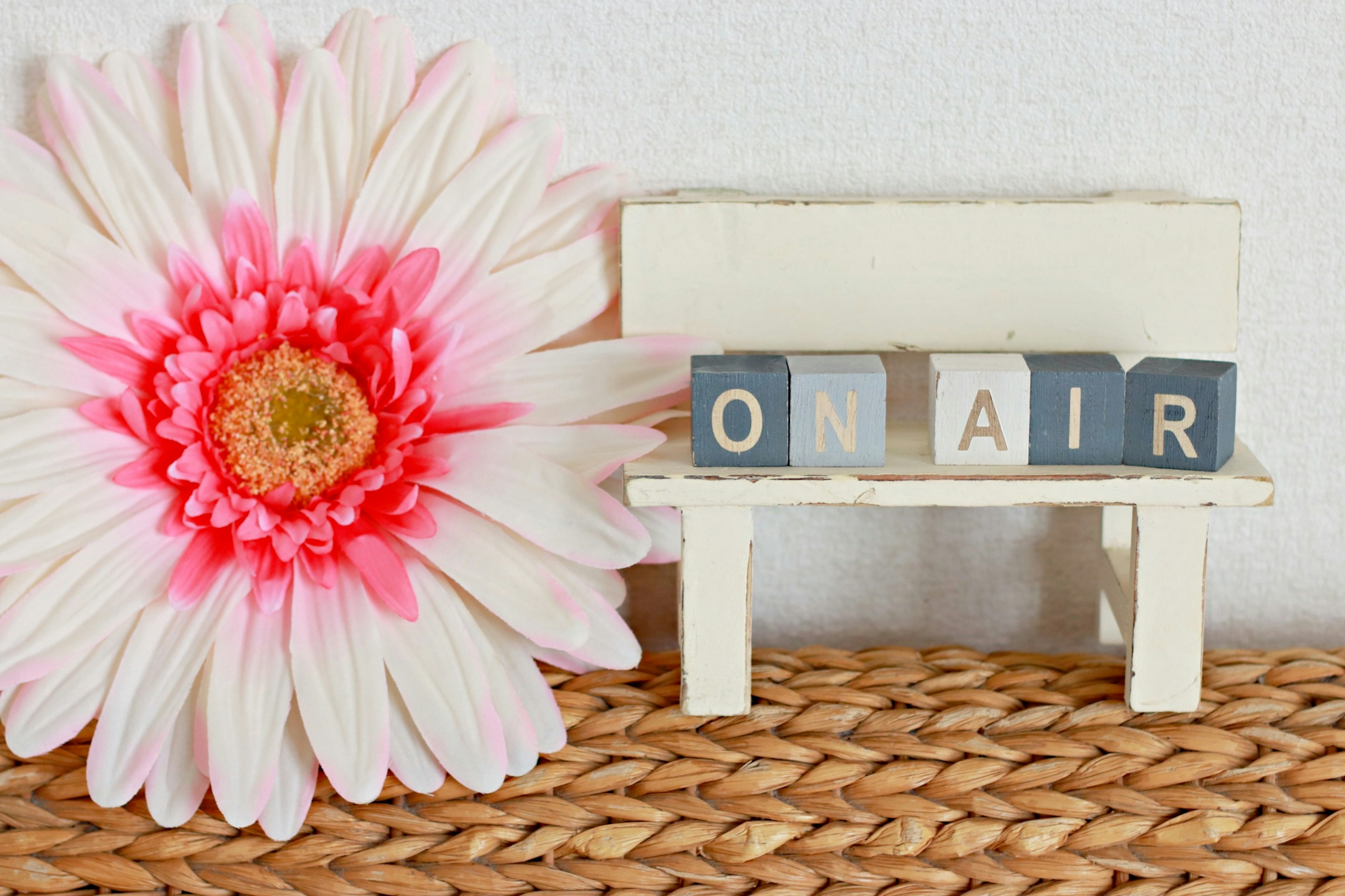 Un petit banc avec des blocs formant 'ON AIR' à côté d'une fleur rose