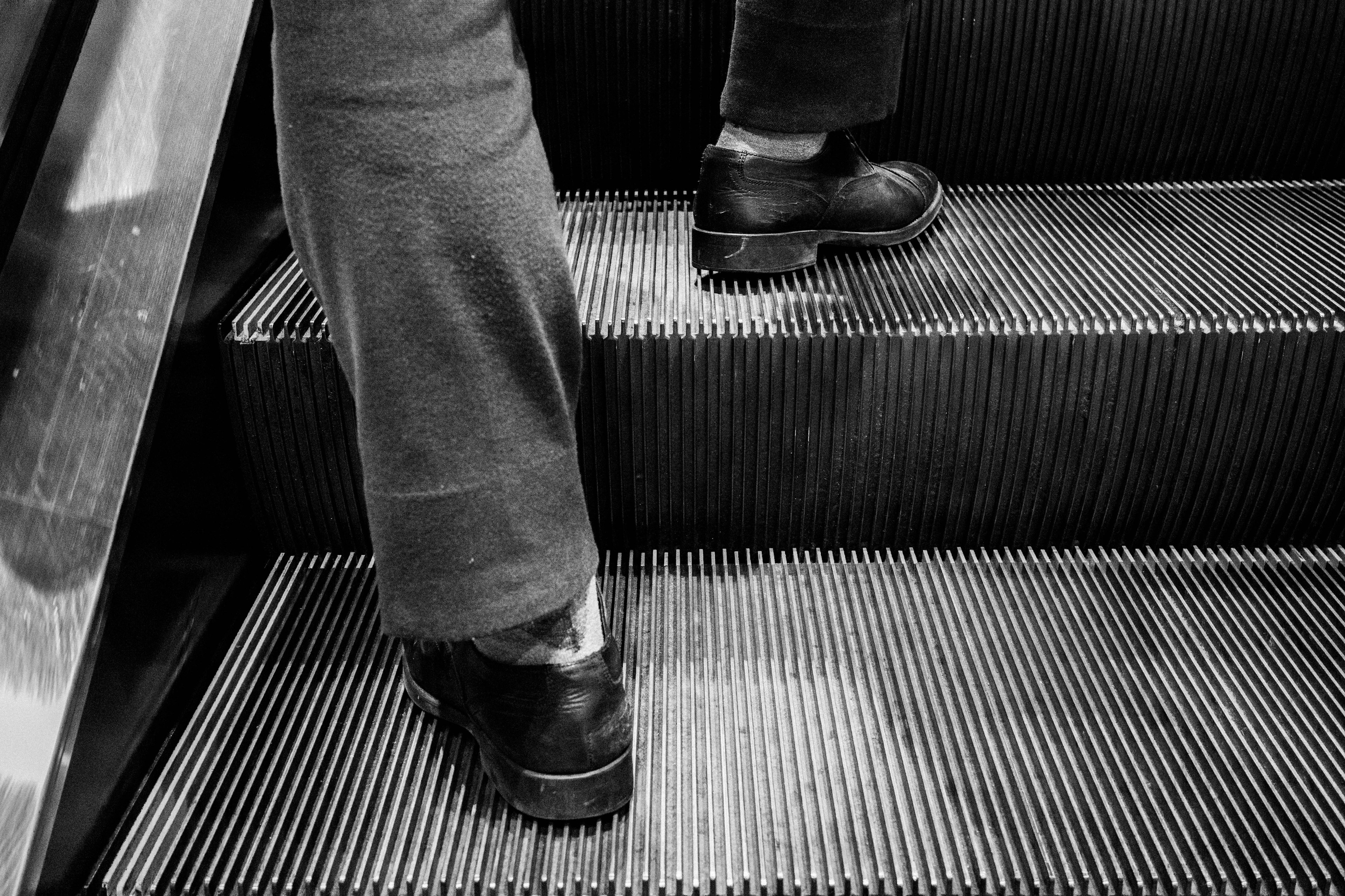 Eine Person mit schwarzen Schuhen, die eine Rolltreppe hinaufsteigt