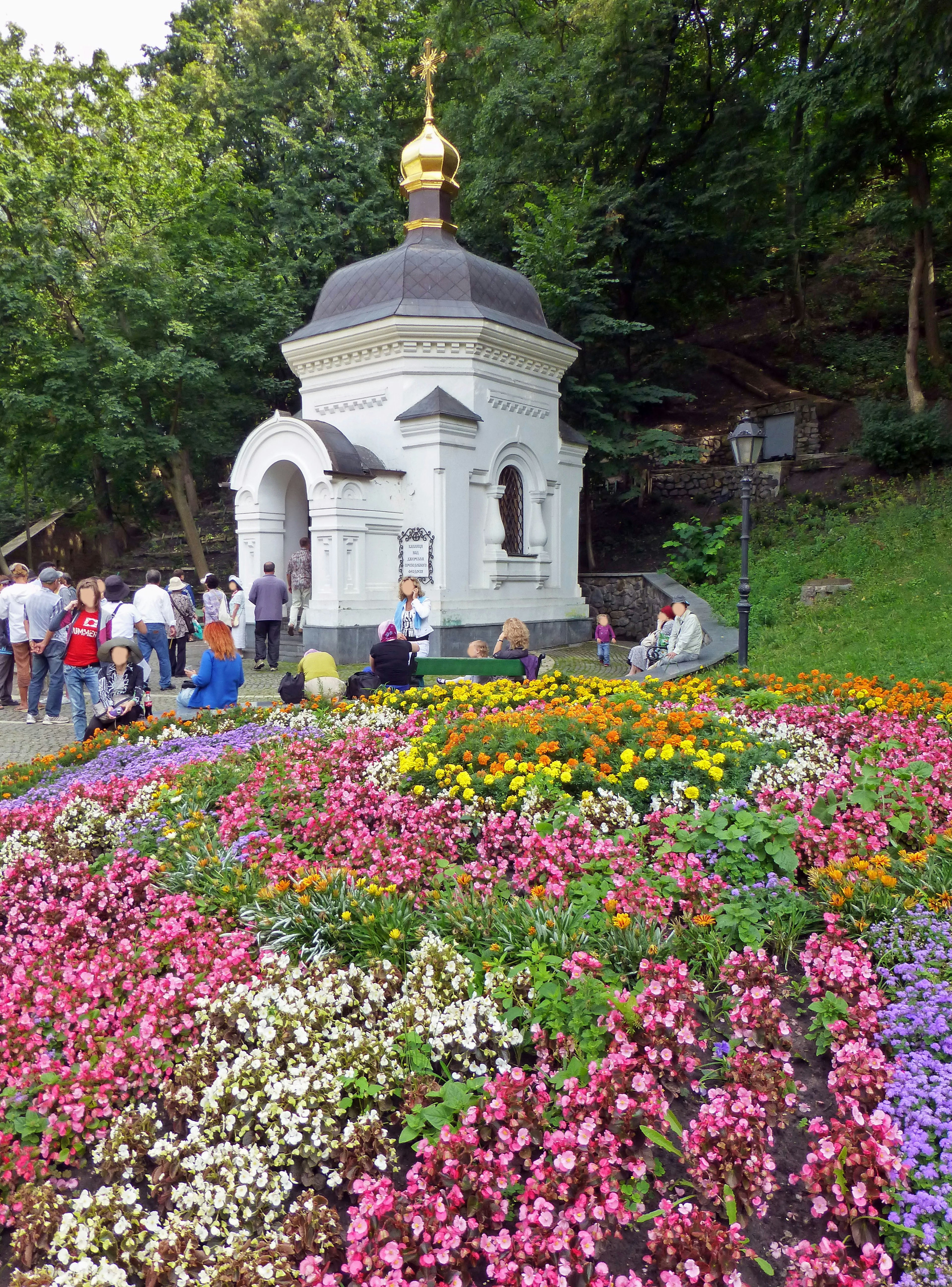 Kleine weiße Kapelle umgeben von bunten Blumen mit Besuchern in der Nähe