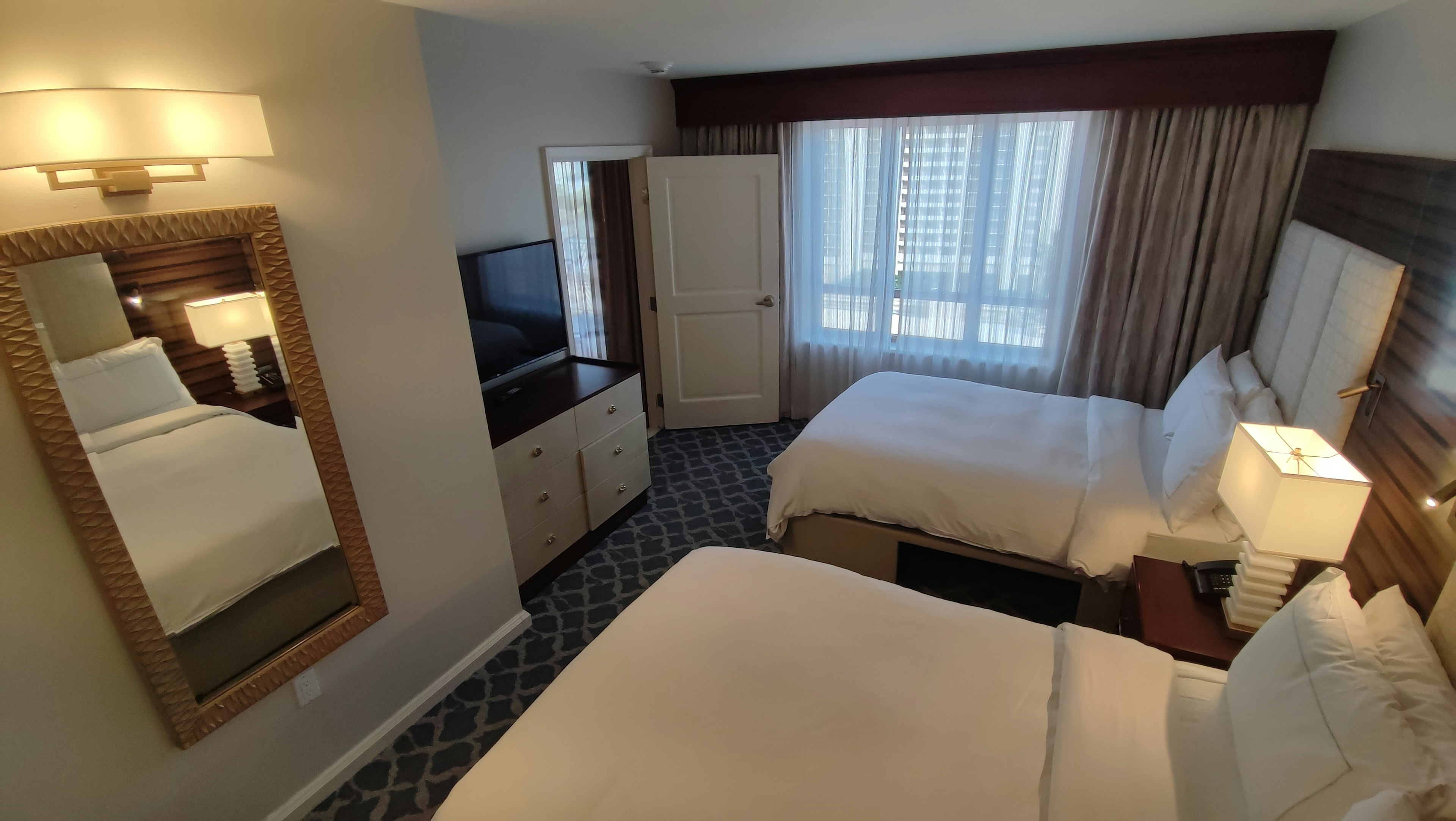 Bright hotel room featuring two beds large window television and mirror