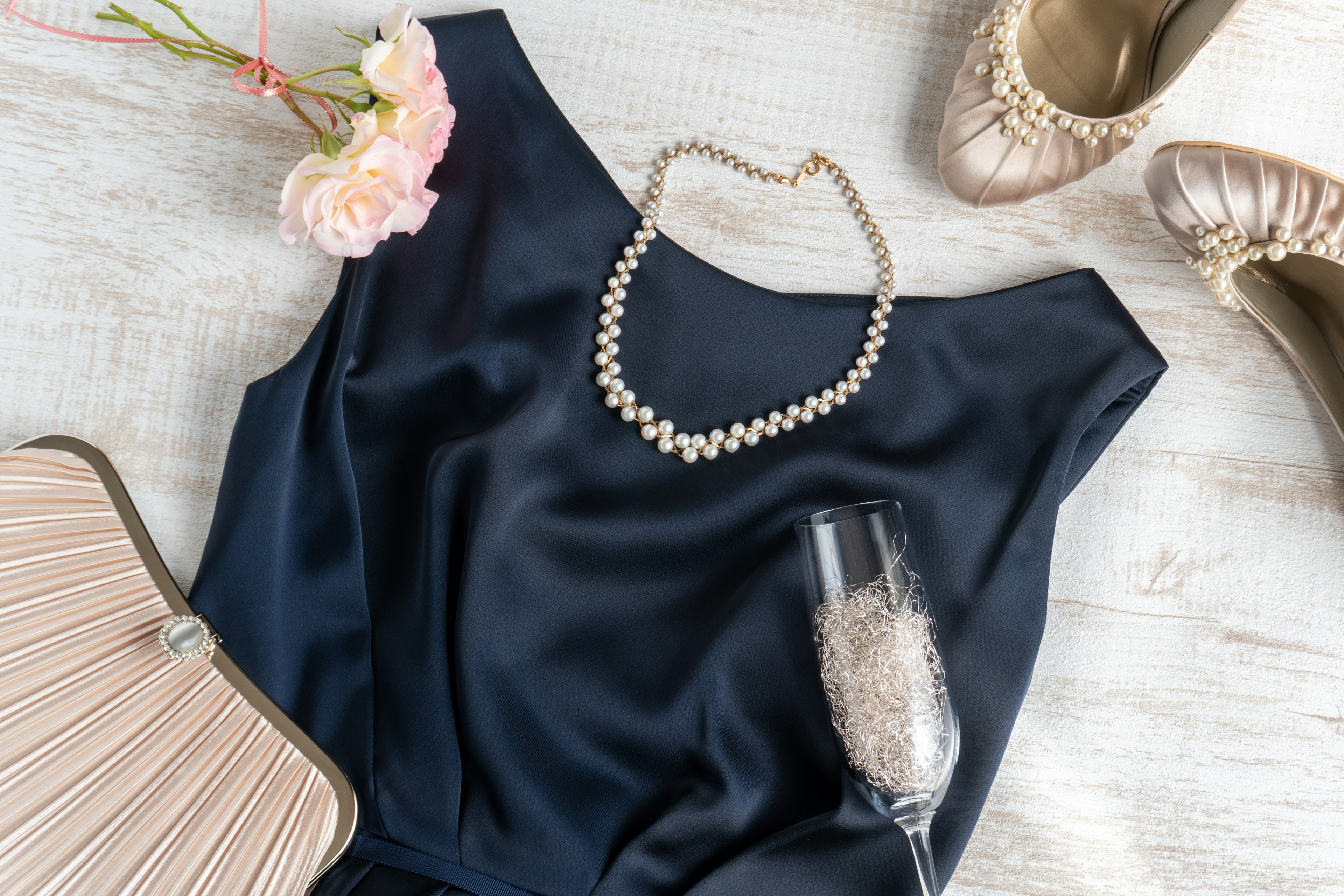 Arrangement élégant avec une robe bleue marine collier de perles verre de champagne fleur et chaussures dorées