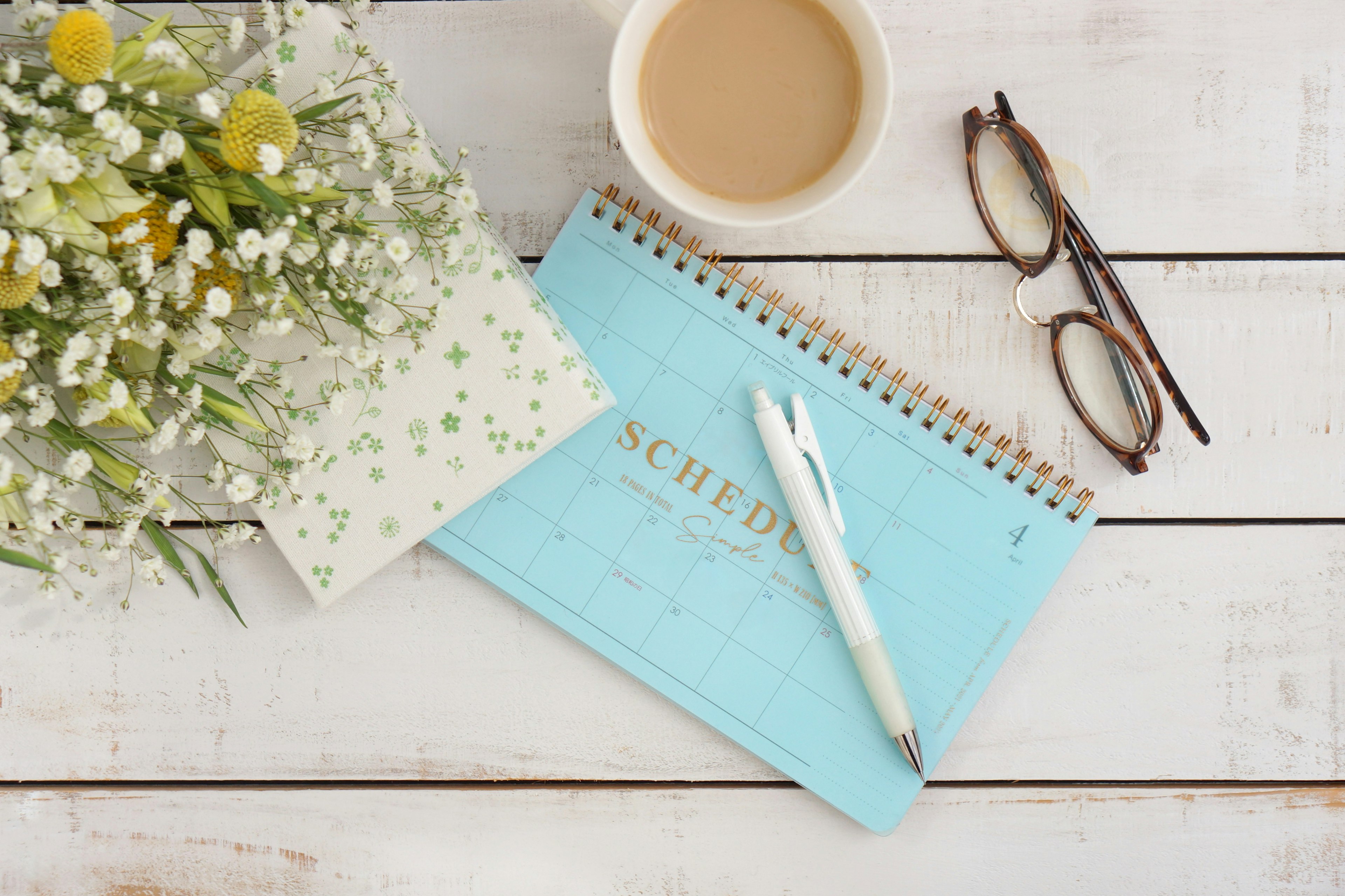 Carnet bleu et stylo avec tasse de café lunettes et bouquet sur une table