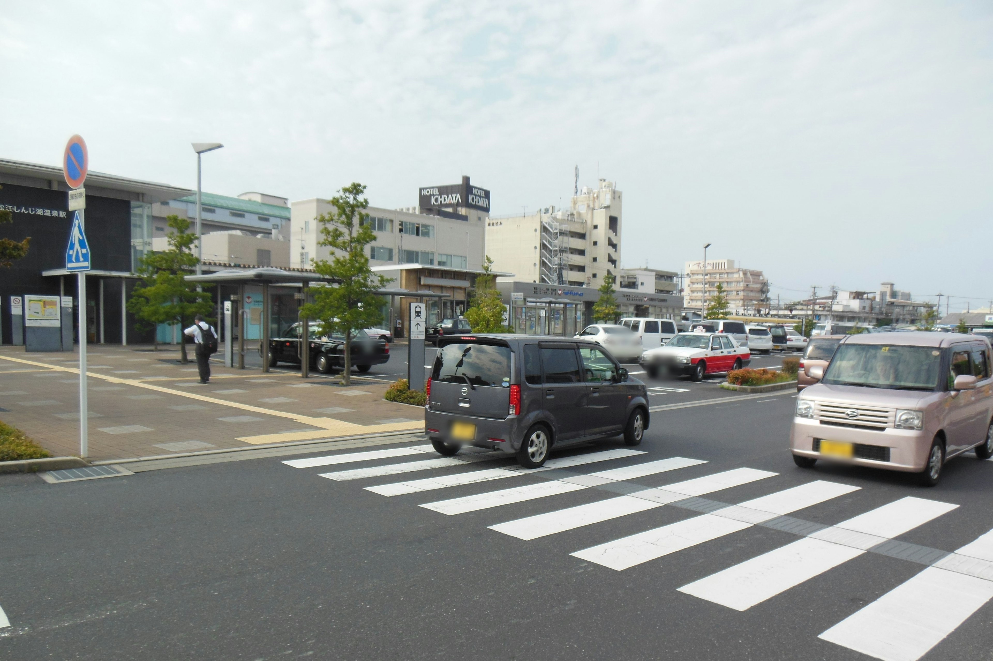 Straßenszene mit Fußgängern, die an einem Zebrastreifen überqueren und Autos auf der Straße