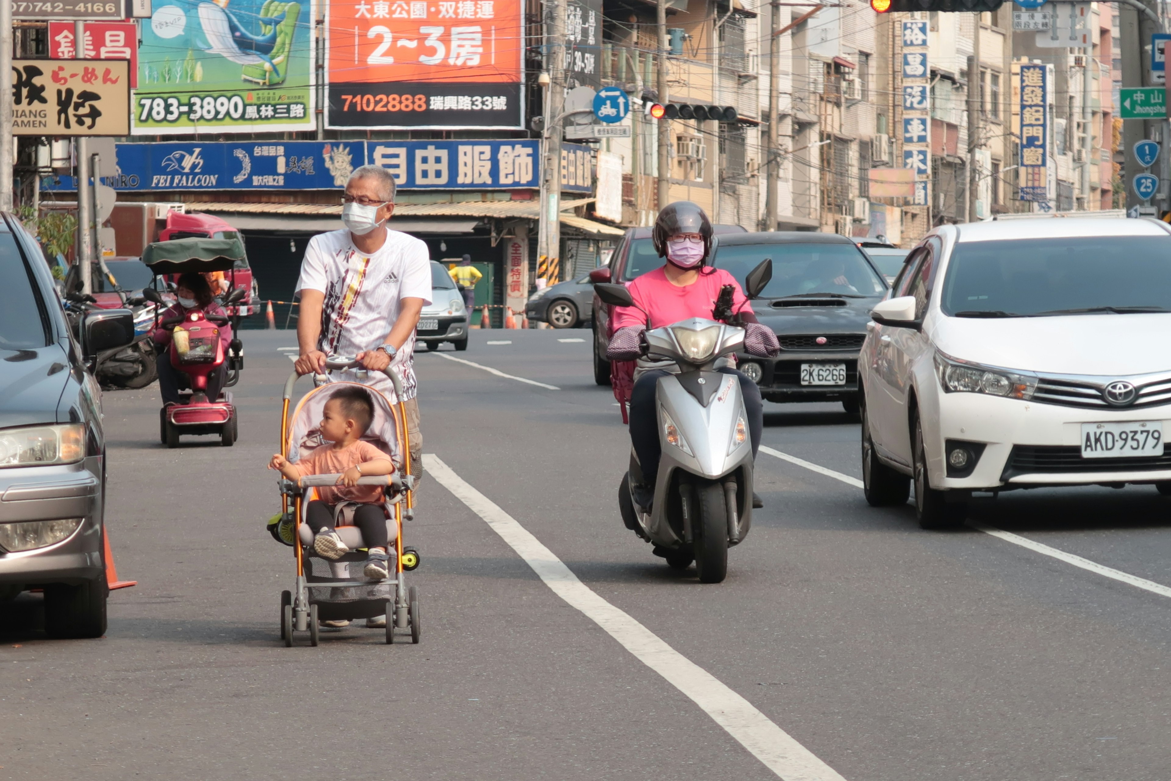 Père poussant un enfant dans une poussette sur une rue animée avec une femme à moto