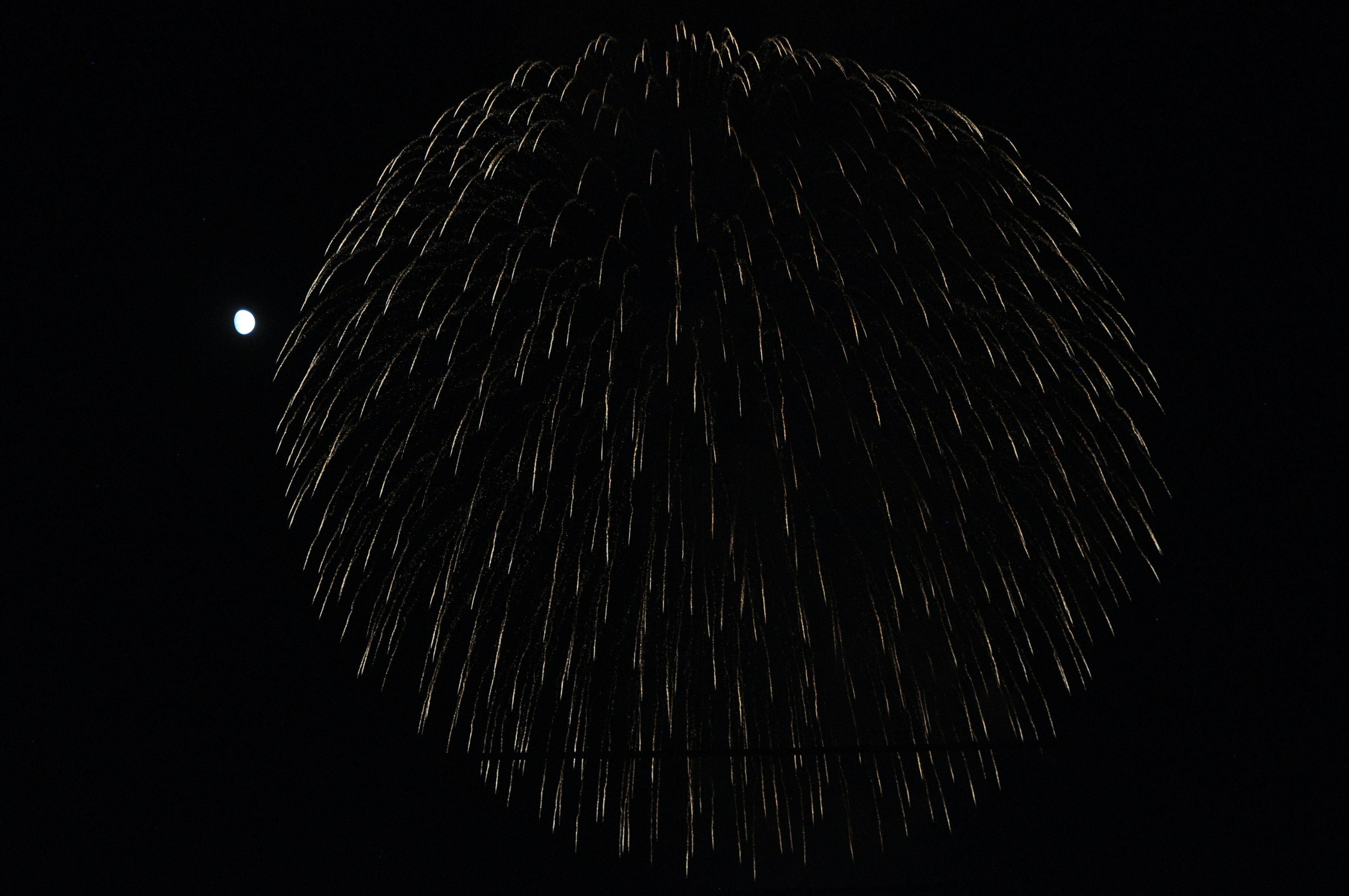 Fireworks display creating a spherical pattern against a dark background with a bright dot nearby