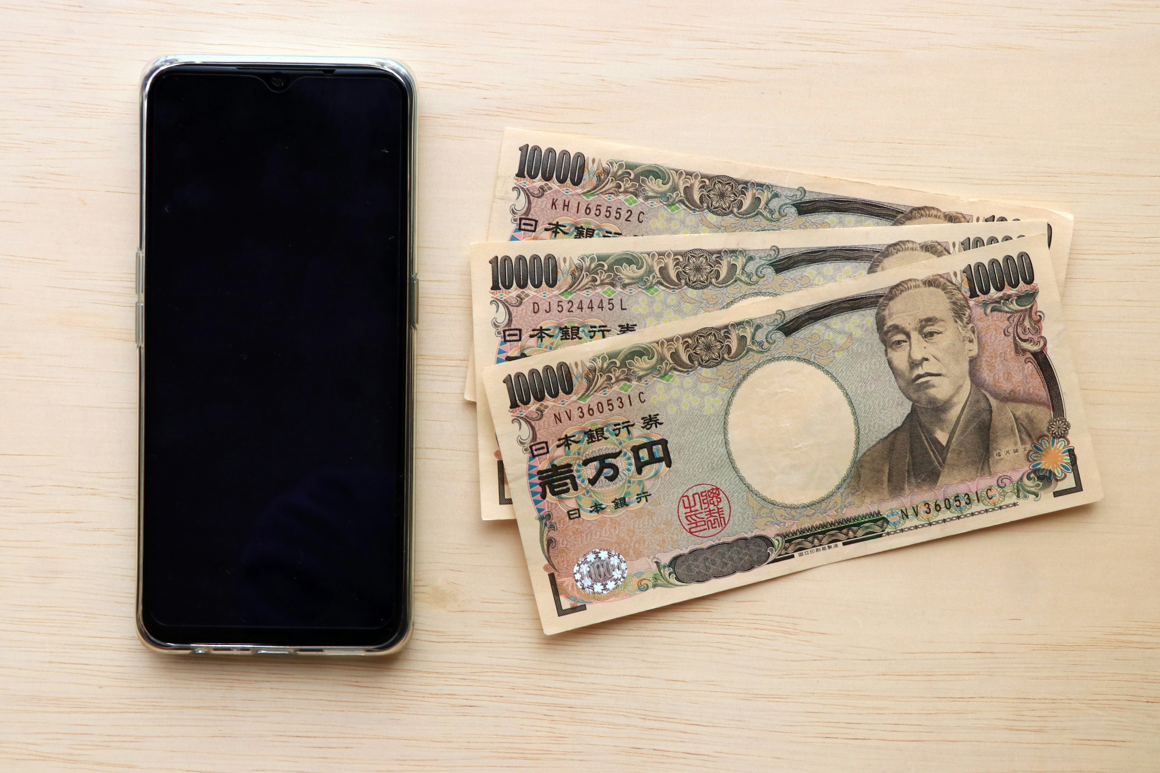 A black smartphone next to Japanese yen banknotes