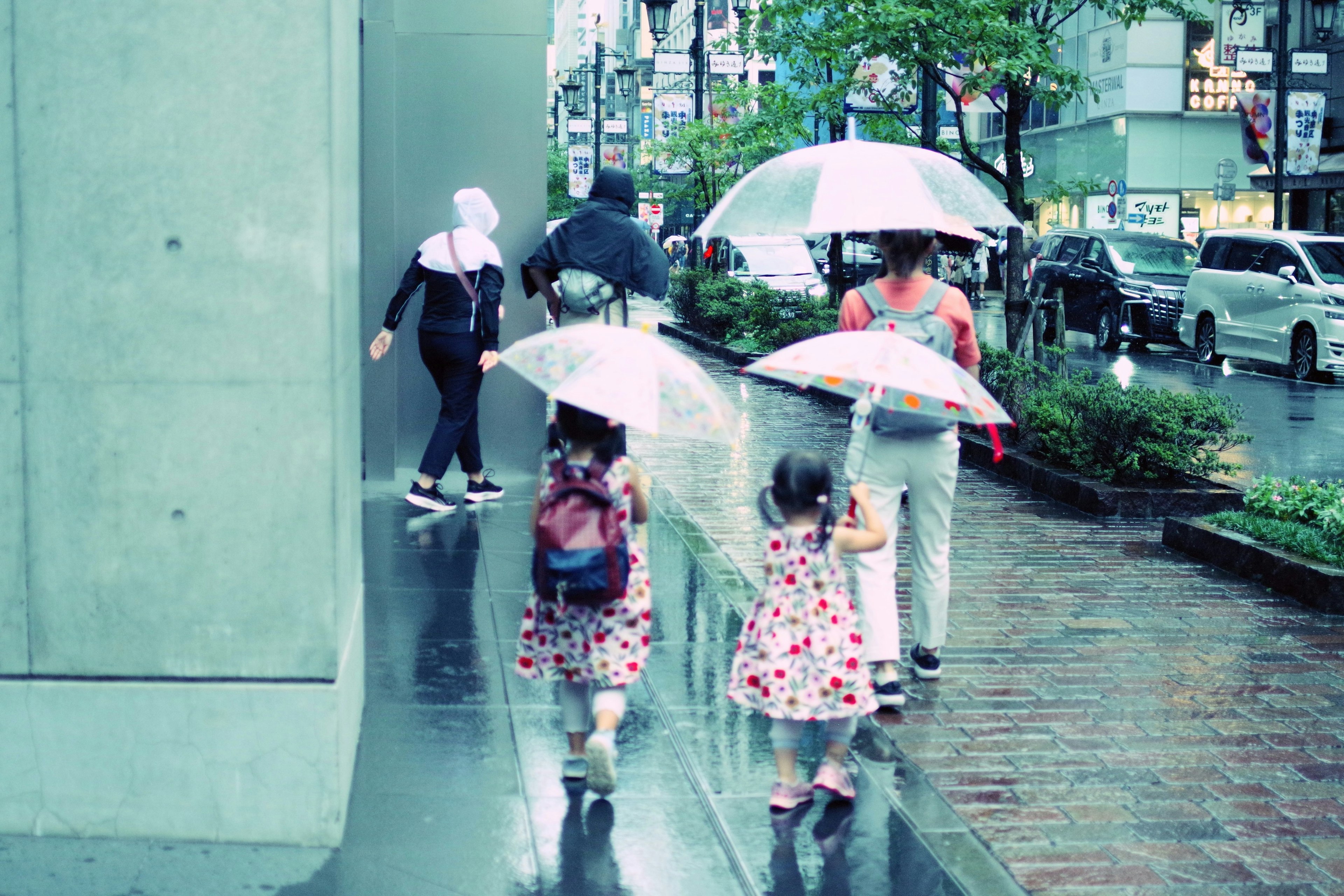 Niños con paraguas caminando bajo la lluvia junto a adultos en un entorno urbano