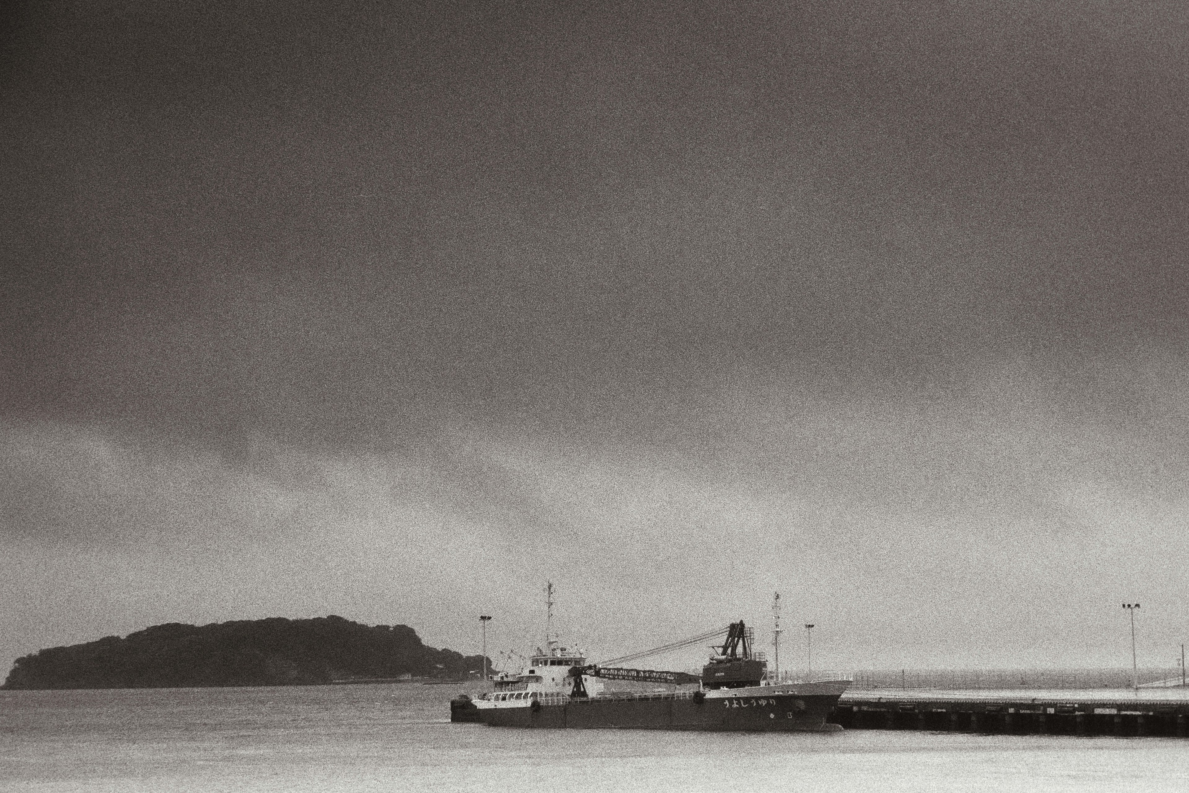 A boat docked at a pier with a distant island under a cloudy sky