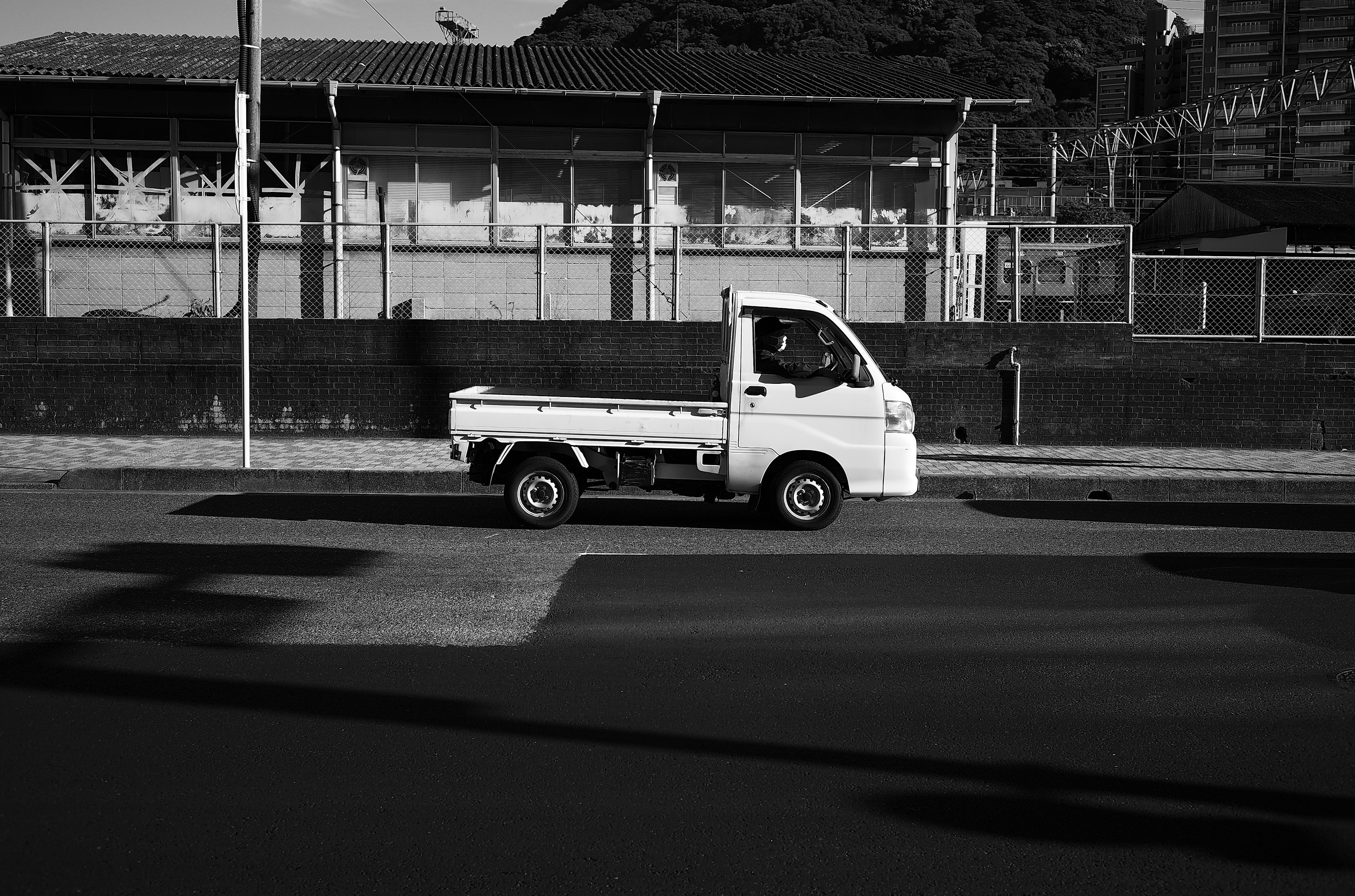 一輛小白色卡車沿著道路行駛，背景是工廠建築