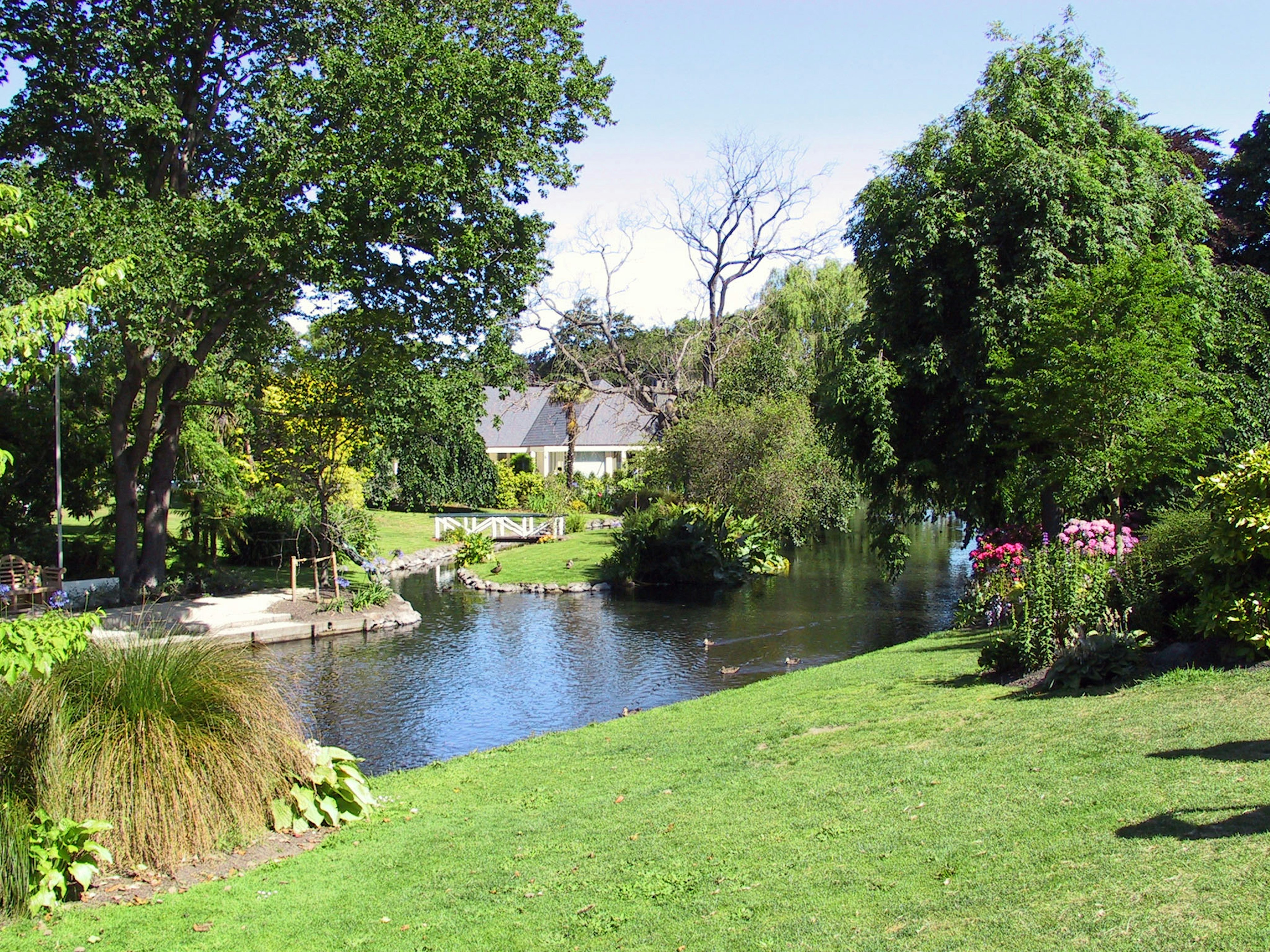 A serene pond with lush gardens surrounding it A house in the background with beautiful nature