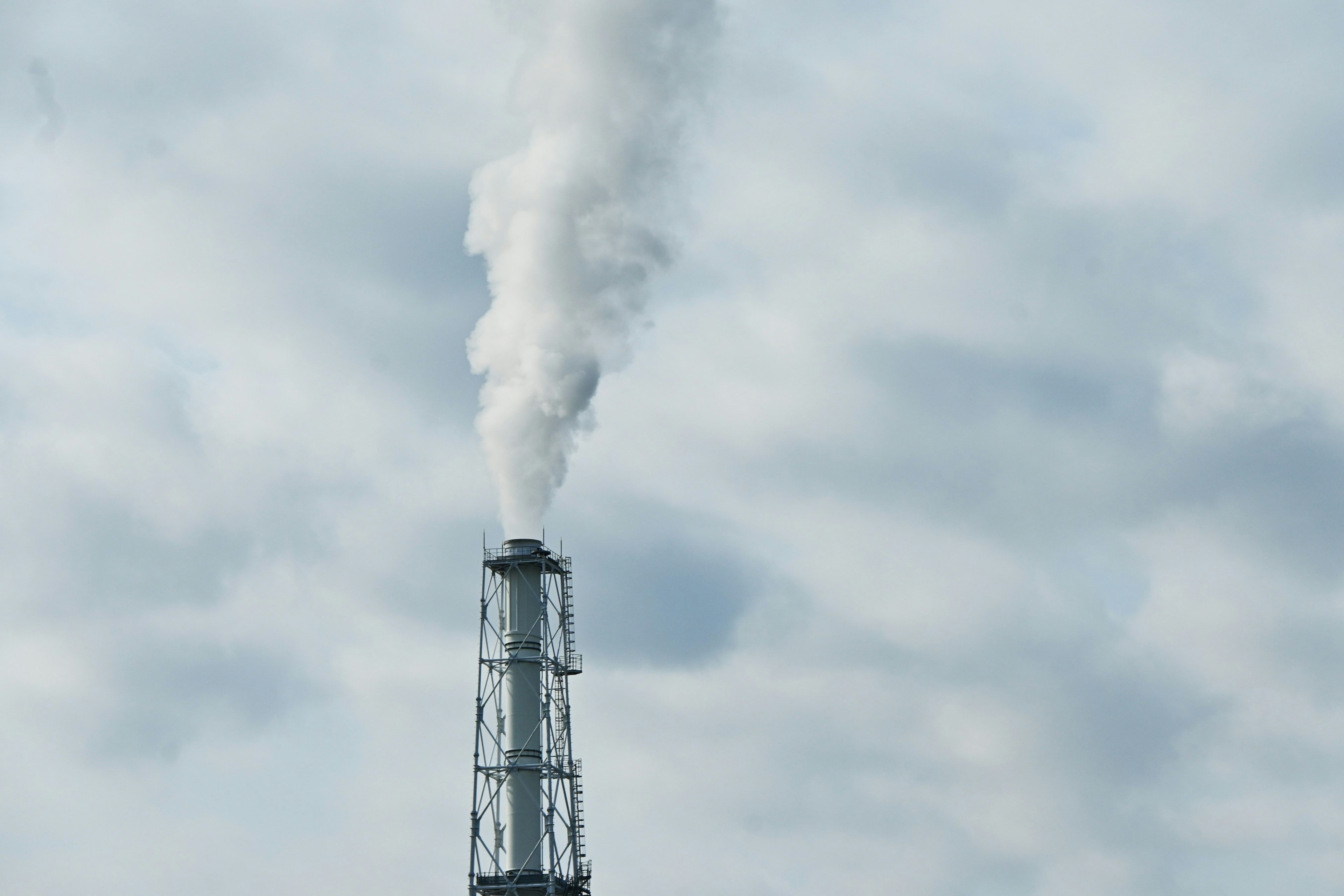 Rauch steigt aus einem Industrie-Schornstein gegen einen bewölkten Himmel