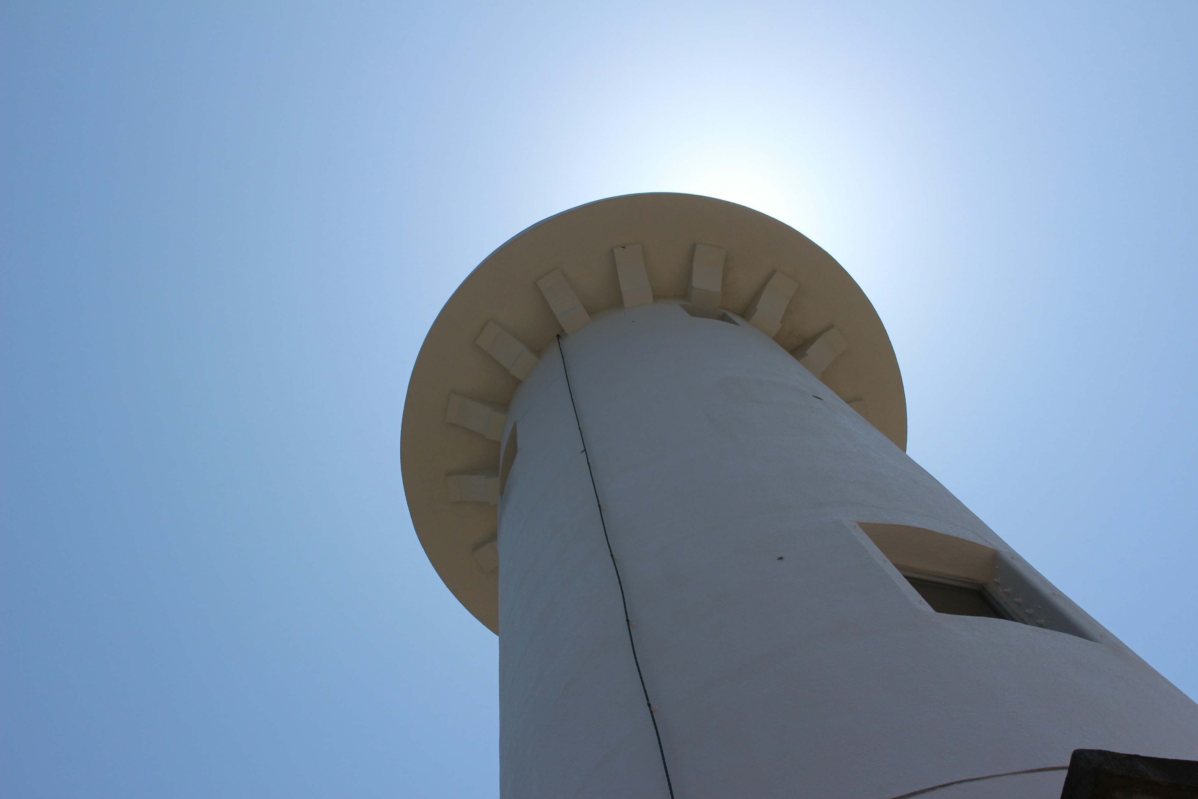 A white lighthouse viewed from below against a clear blue sky