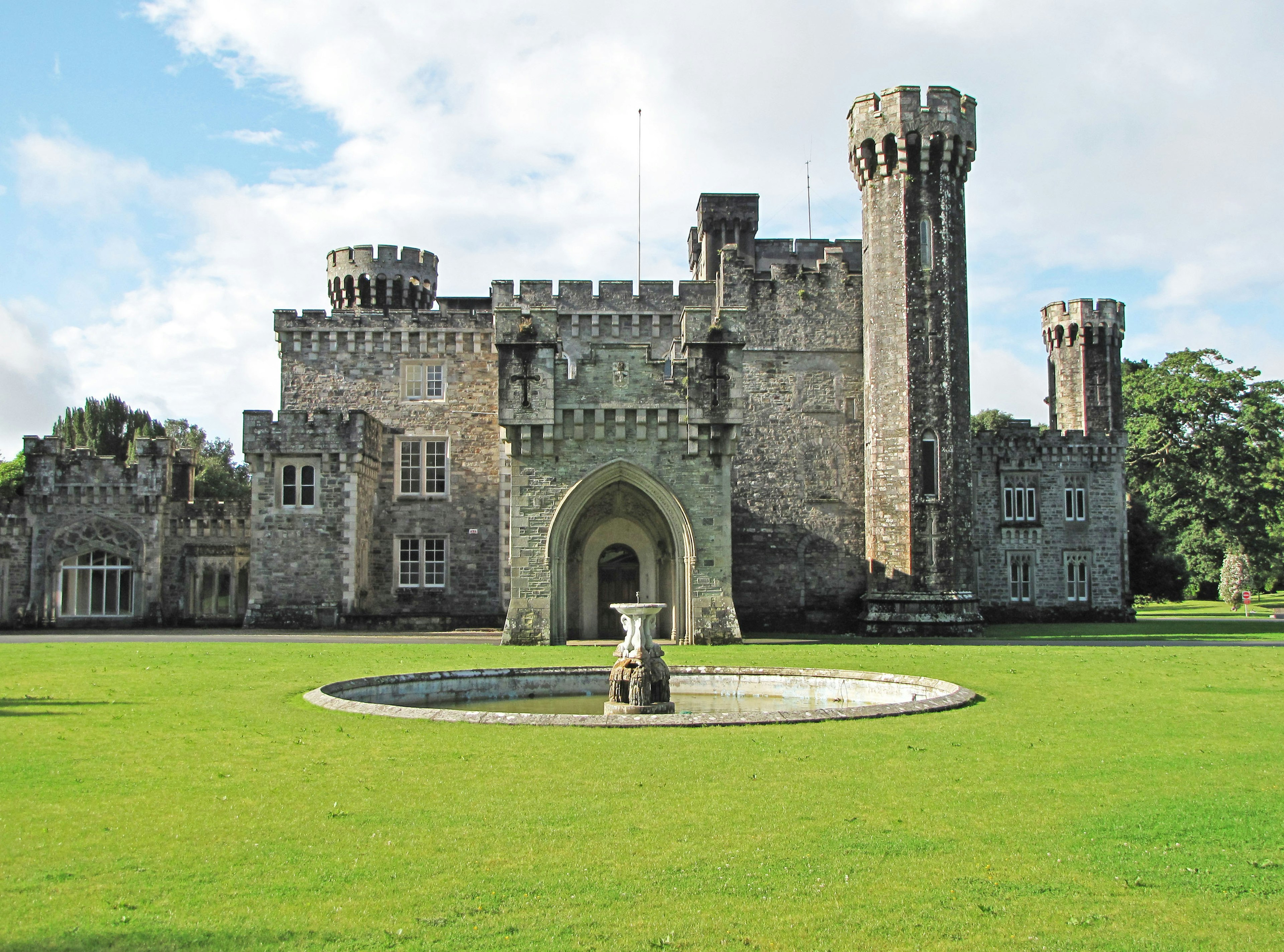 Vista exterior de un castillo de estilo medieval rodeado de césped verde y una fuente