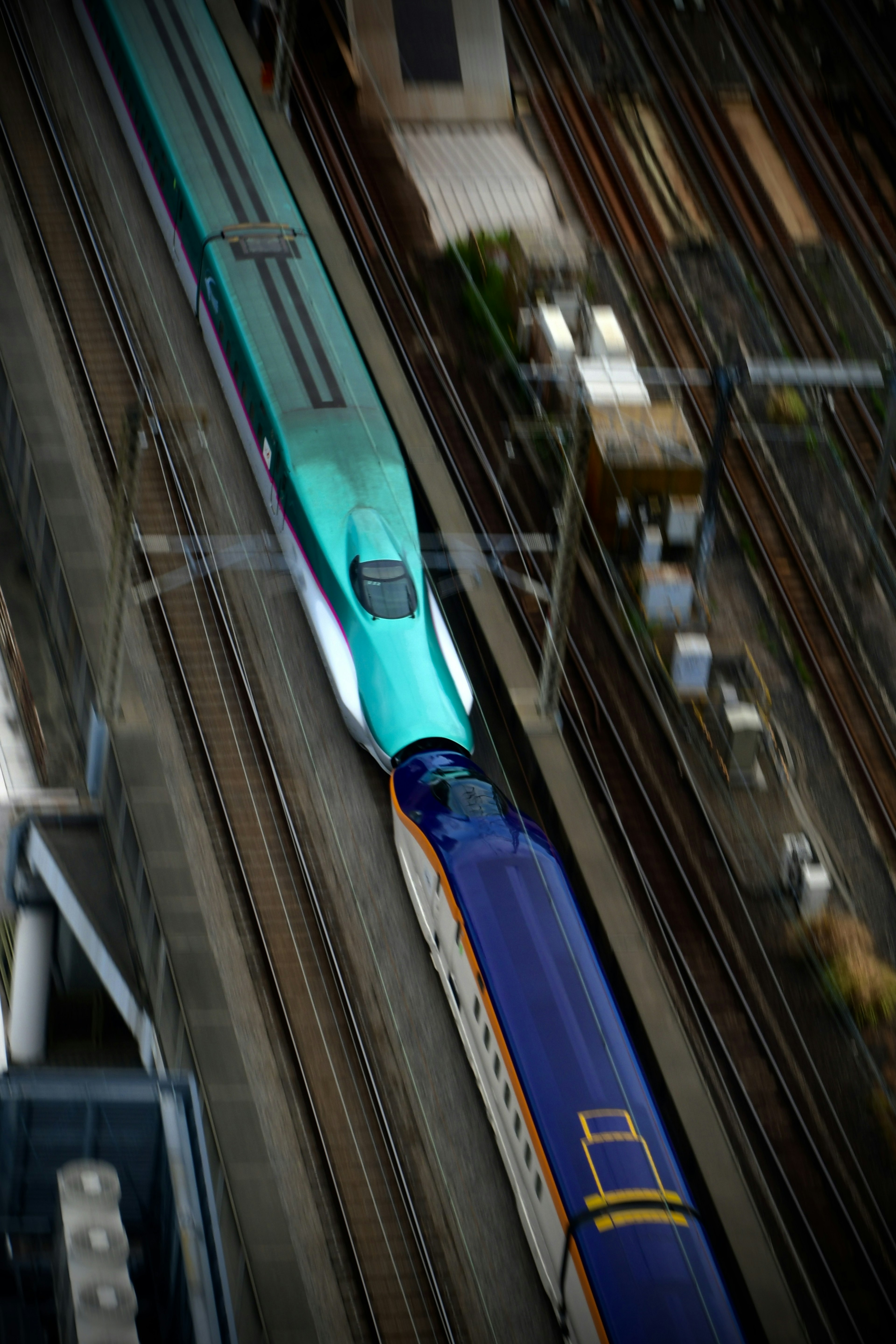 Luftaufnahme eines grünen Shinkansen und eines blauen Zuges, die sich auf Schienen kreuzen