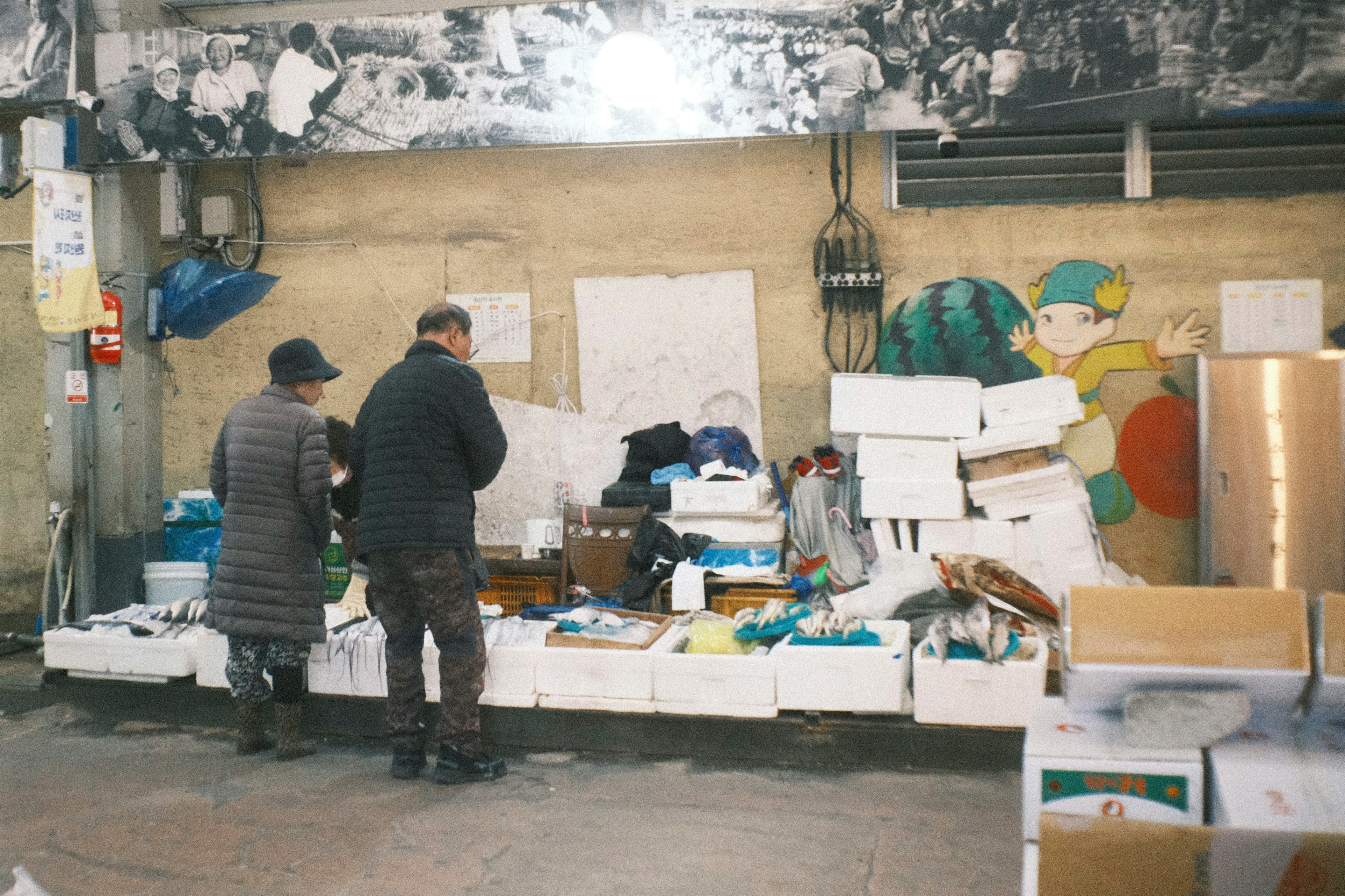 Two men working in front of boxes with colorful artwork on the wall