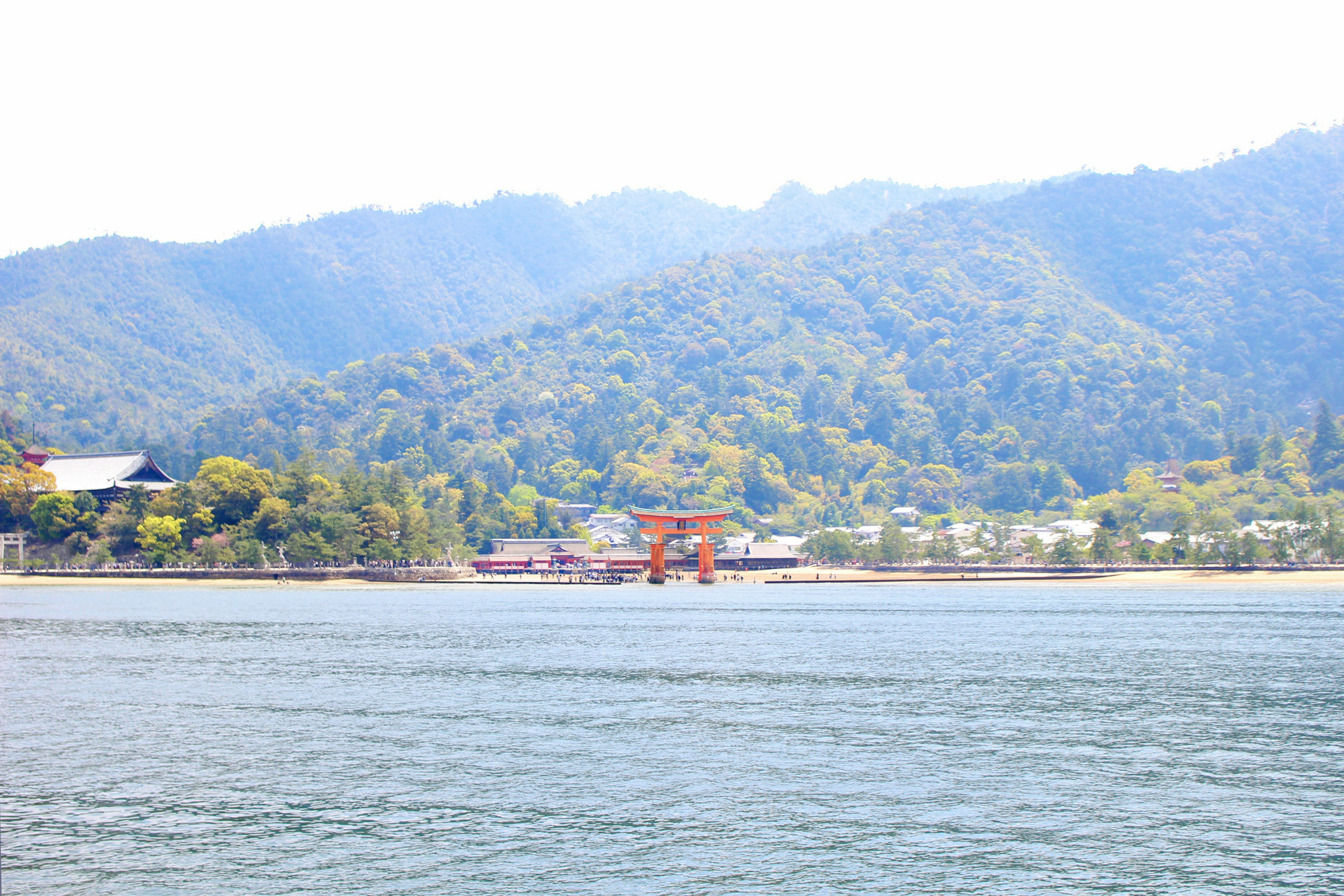 Vista escénica del torii del santuario de Itsukushima con montañas verdes de fondo