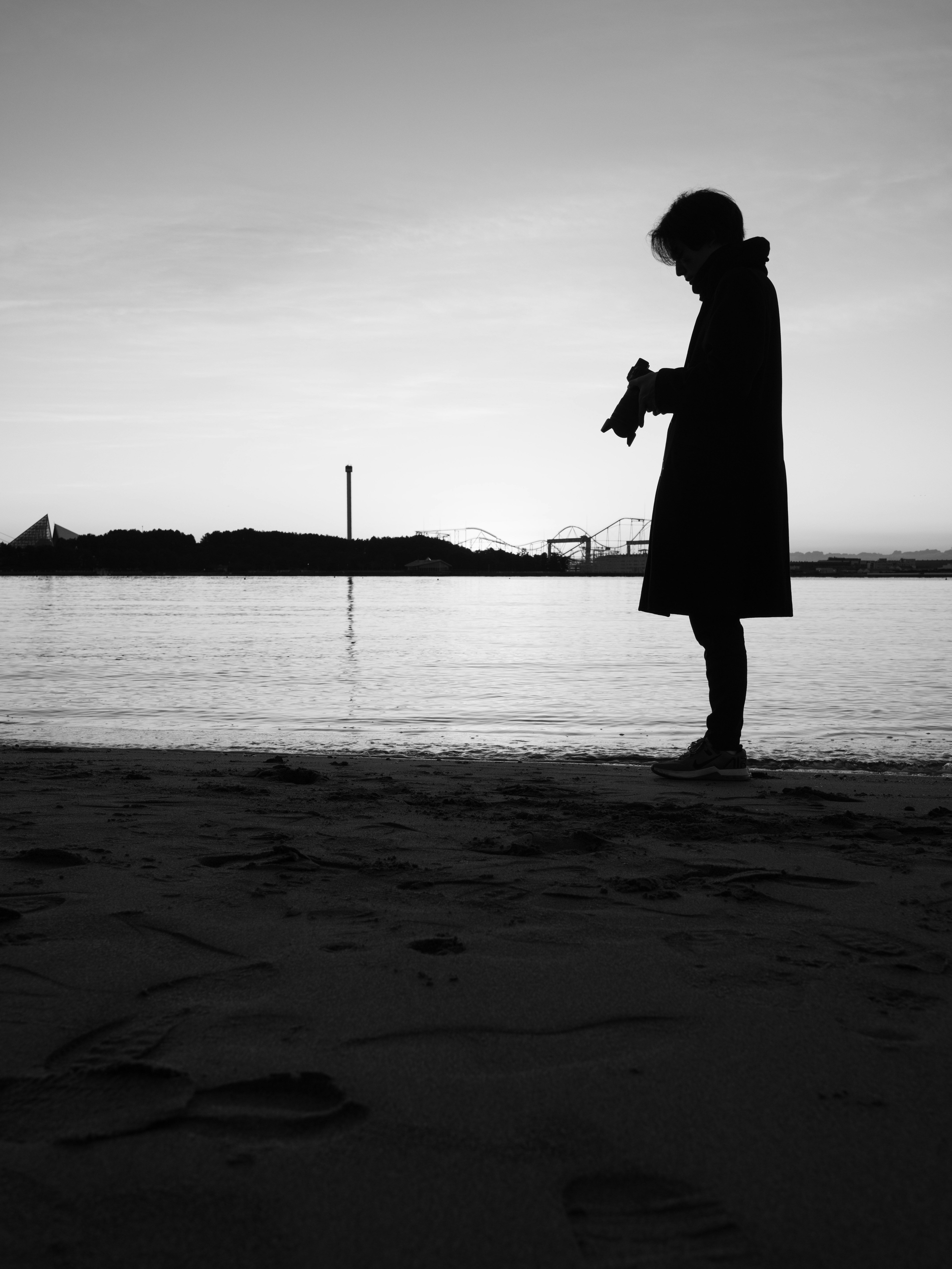 海辺で立つ人物のシルエット 黒と白のコントラストが強い 夕暮れの空と水面が映る