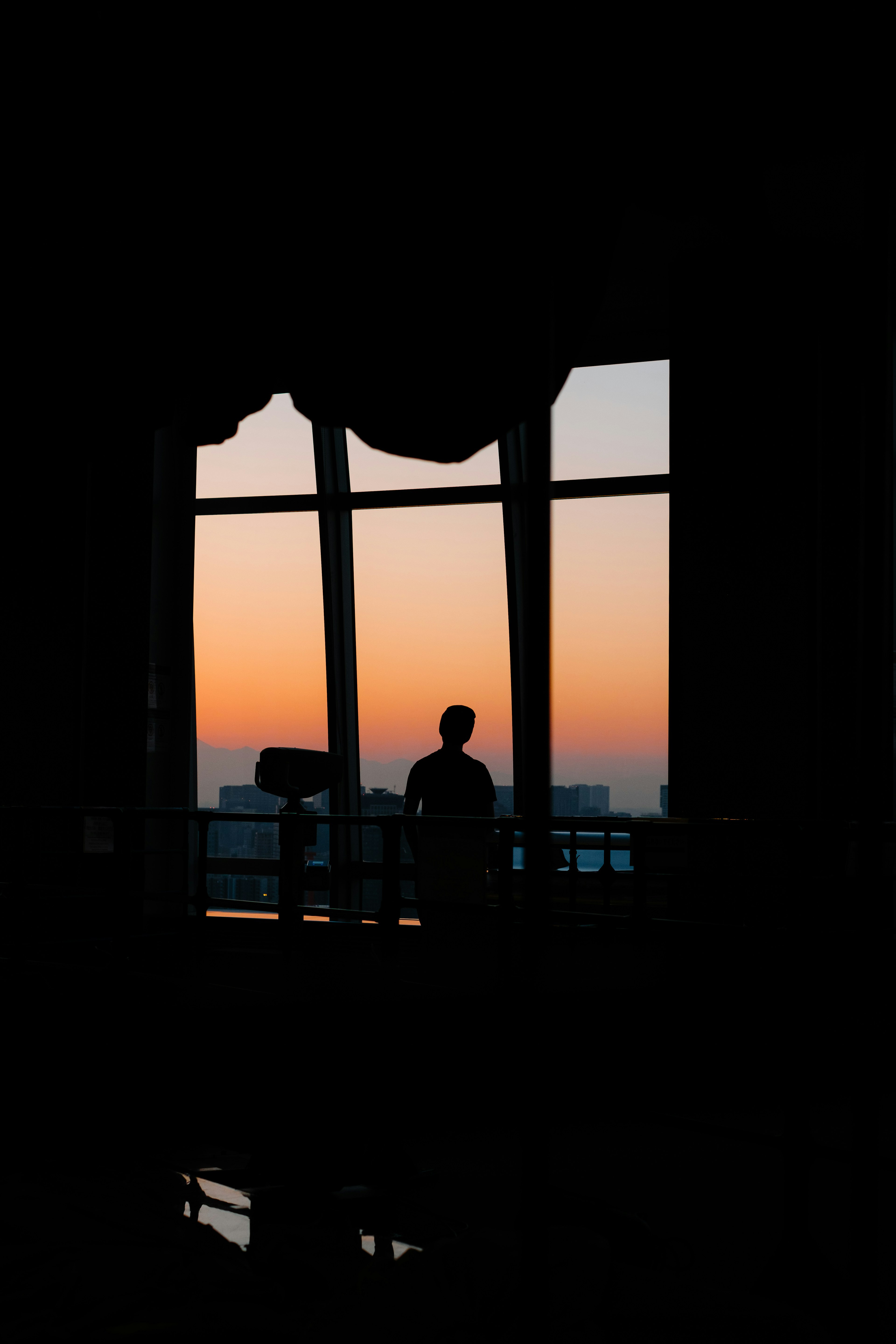 Silueta de una persona de pie contra una vista de atardecer a través de una ventana