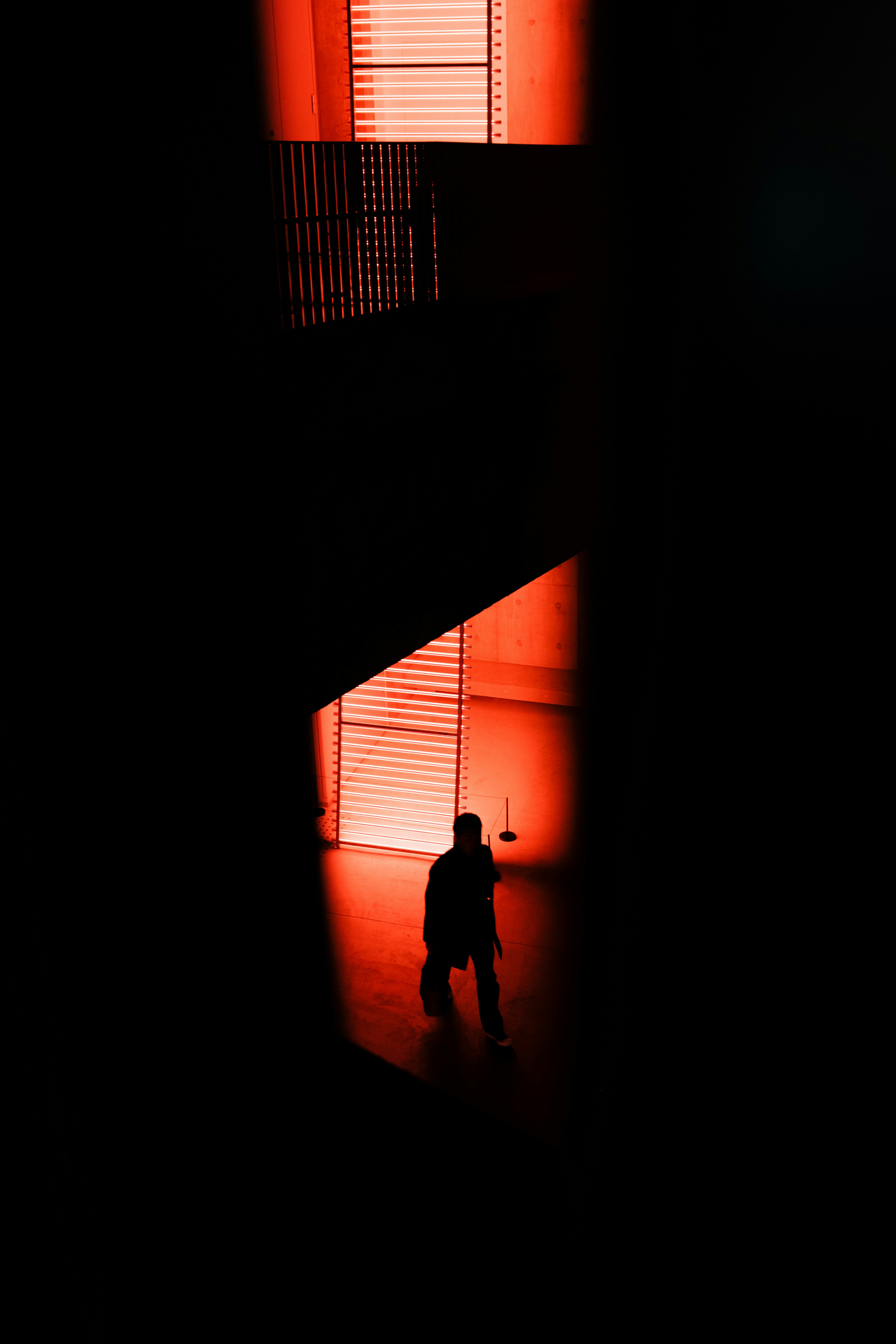 Silhouette d'une personne descendant un escalier illuminé par une lumière rouge