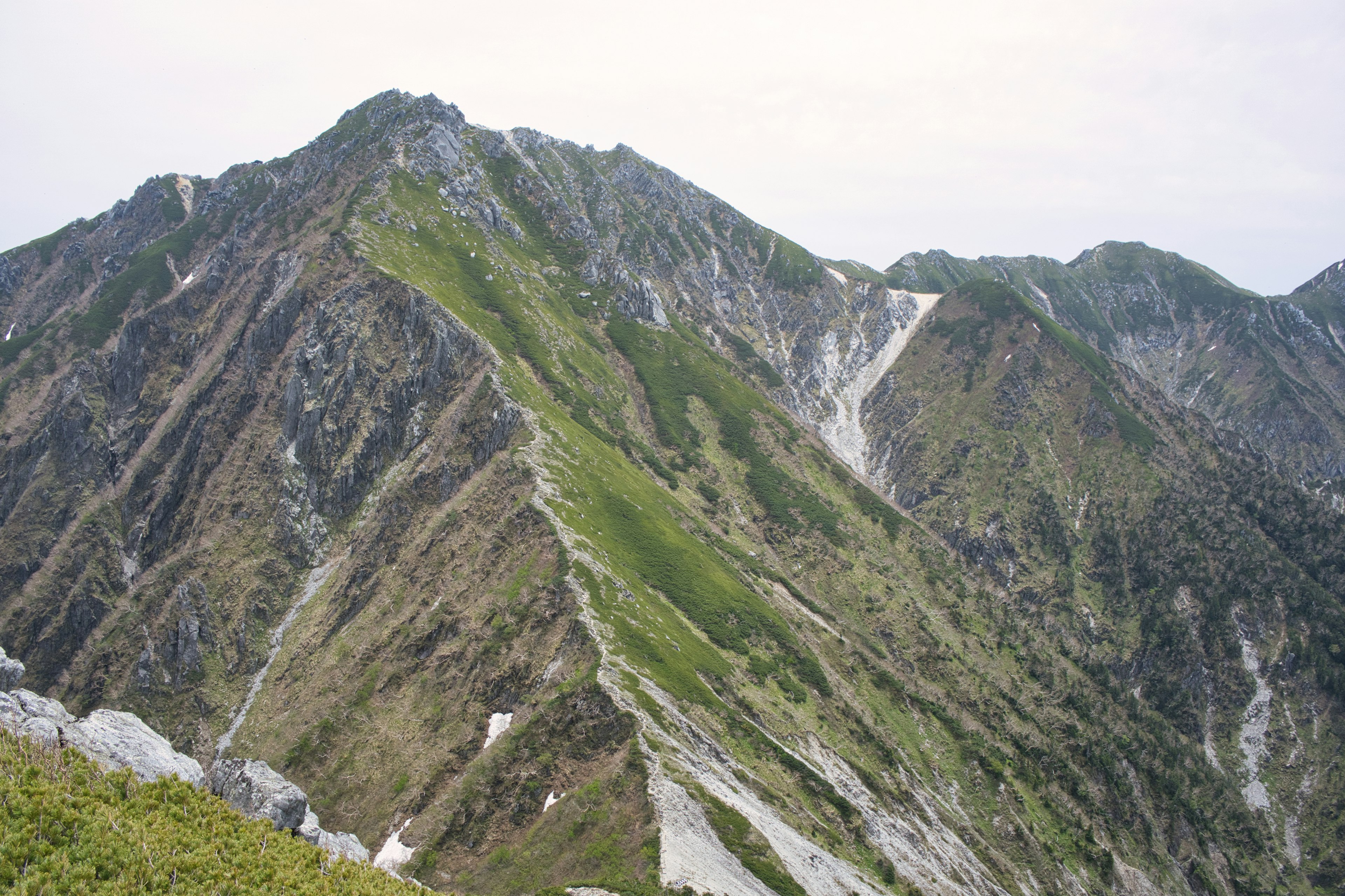 Paisaje montañoso con picos rocosos empinados y laderas verdes