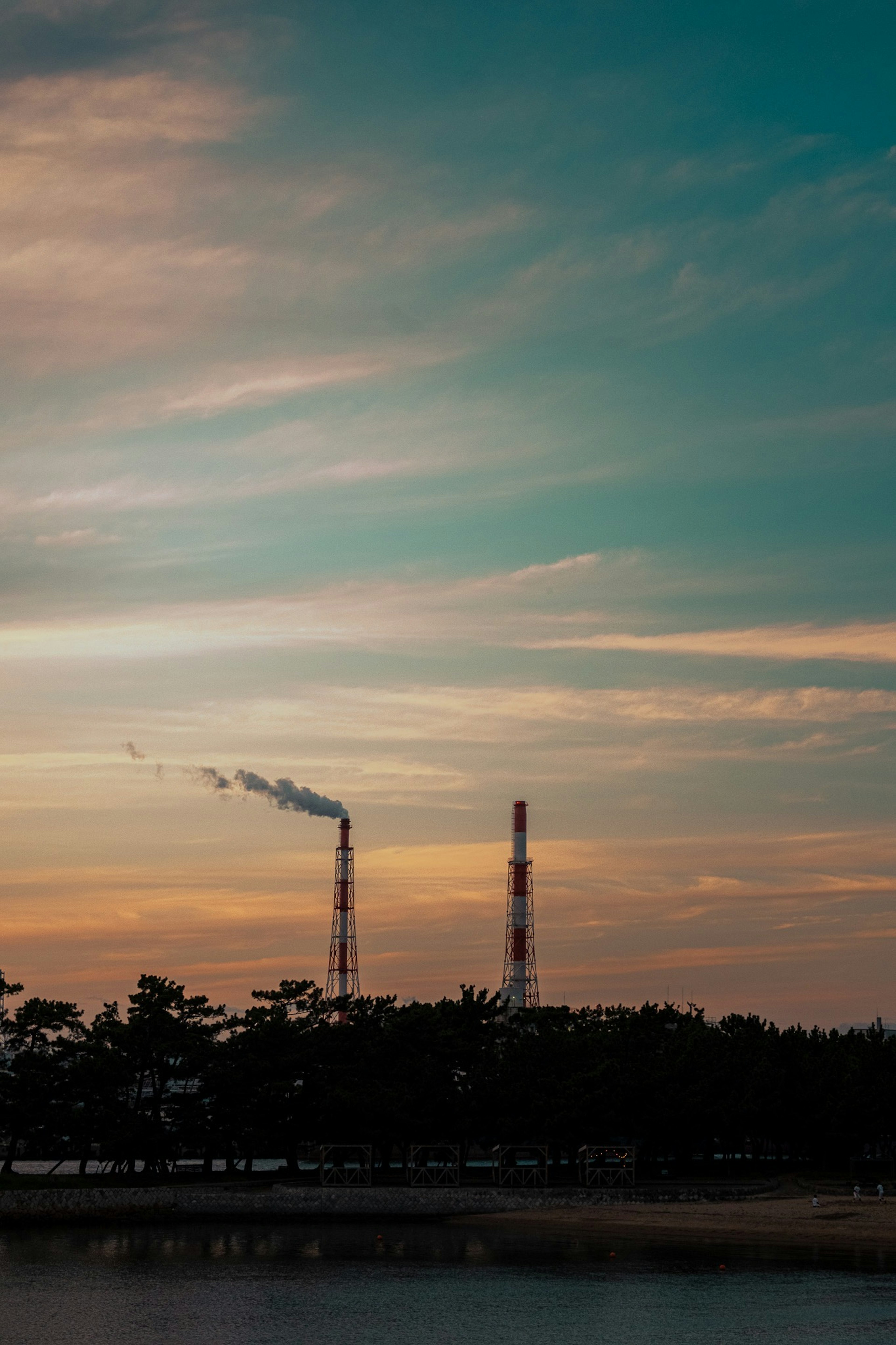 Landscape featuring factory smokestacks emitting smoke against a sunset sky