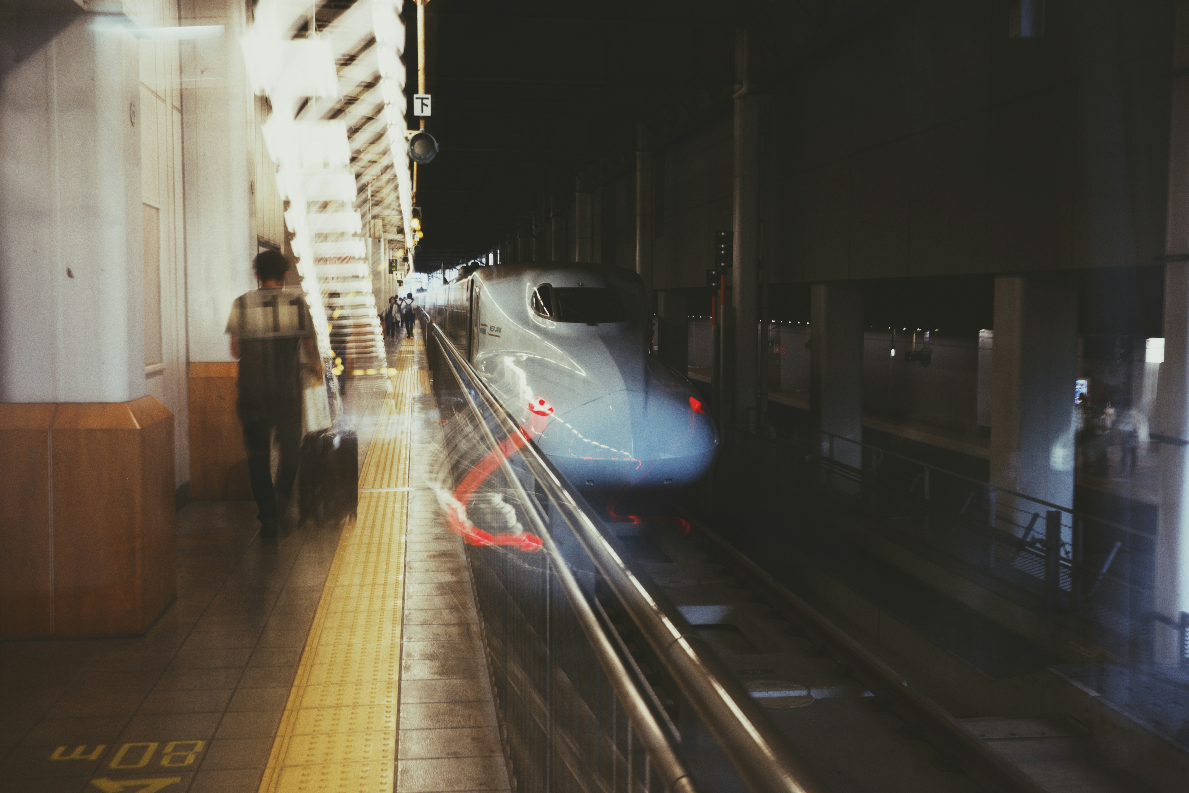 夜の駅で電車が通過する様子と人影