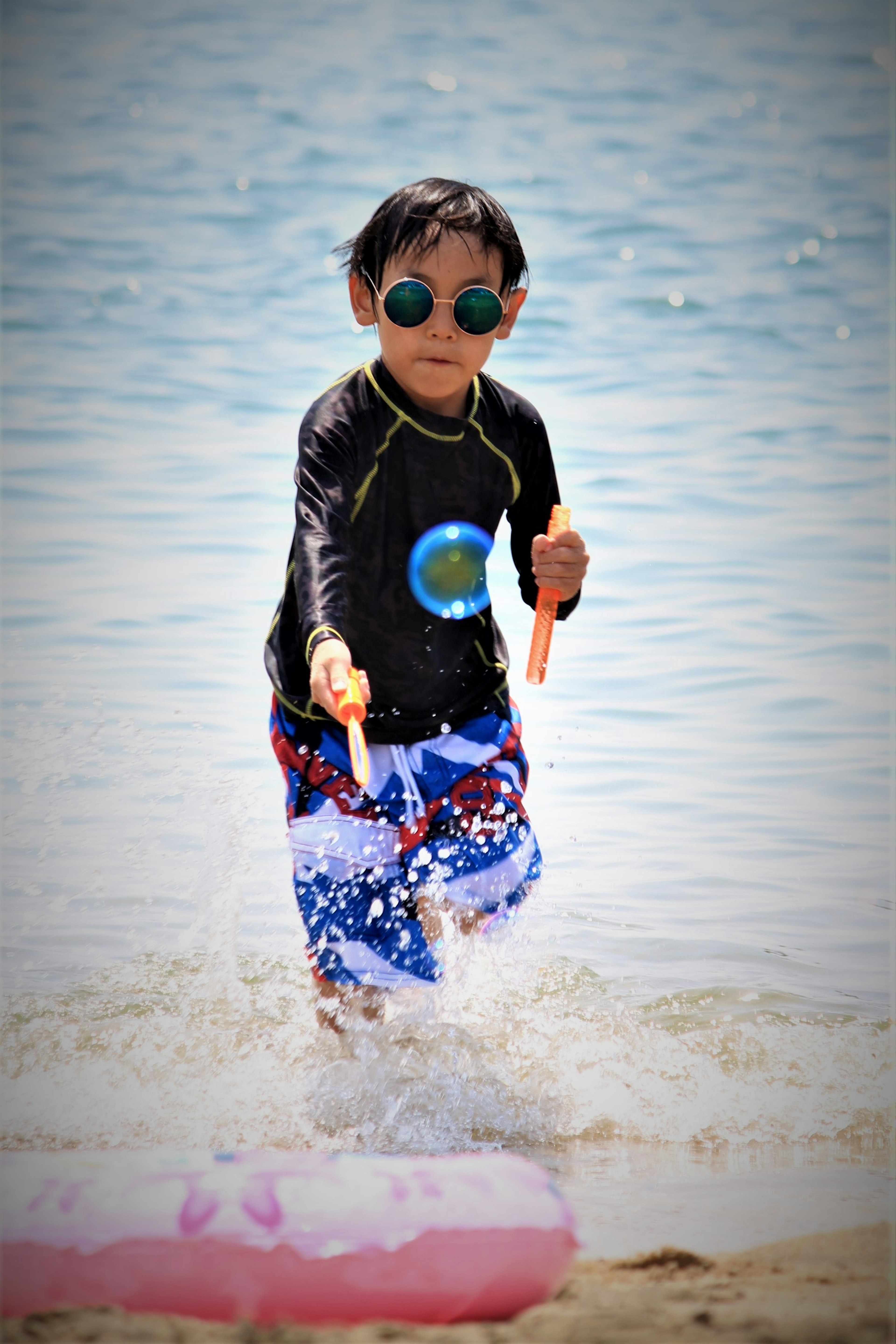 Enfant jouant au bord de l'eau avec des lunettes de soleil et un maillot de bain