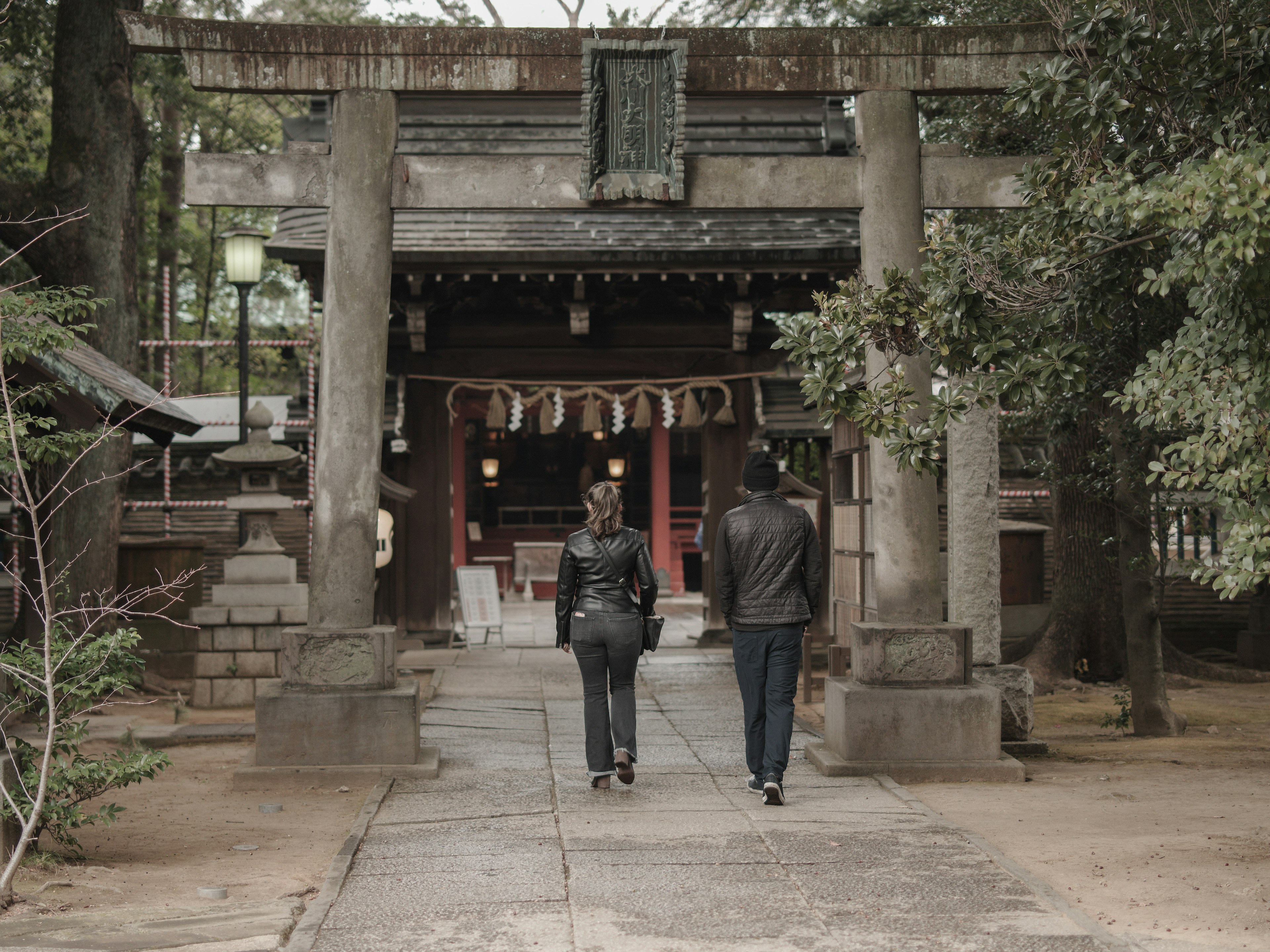 兩個人走向一個神社，古老的石門和郁郁蔥蔥的綠意