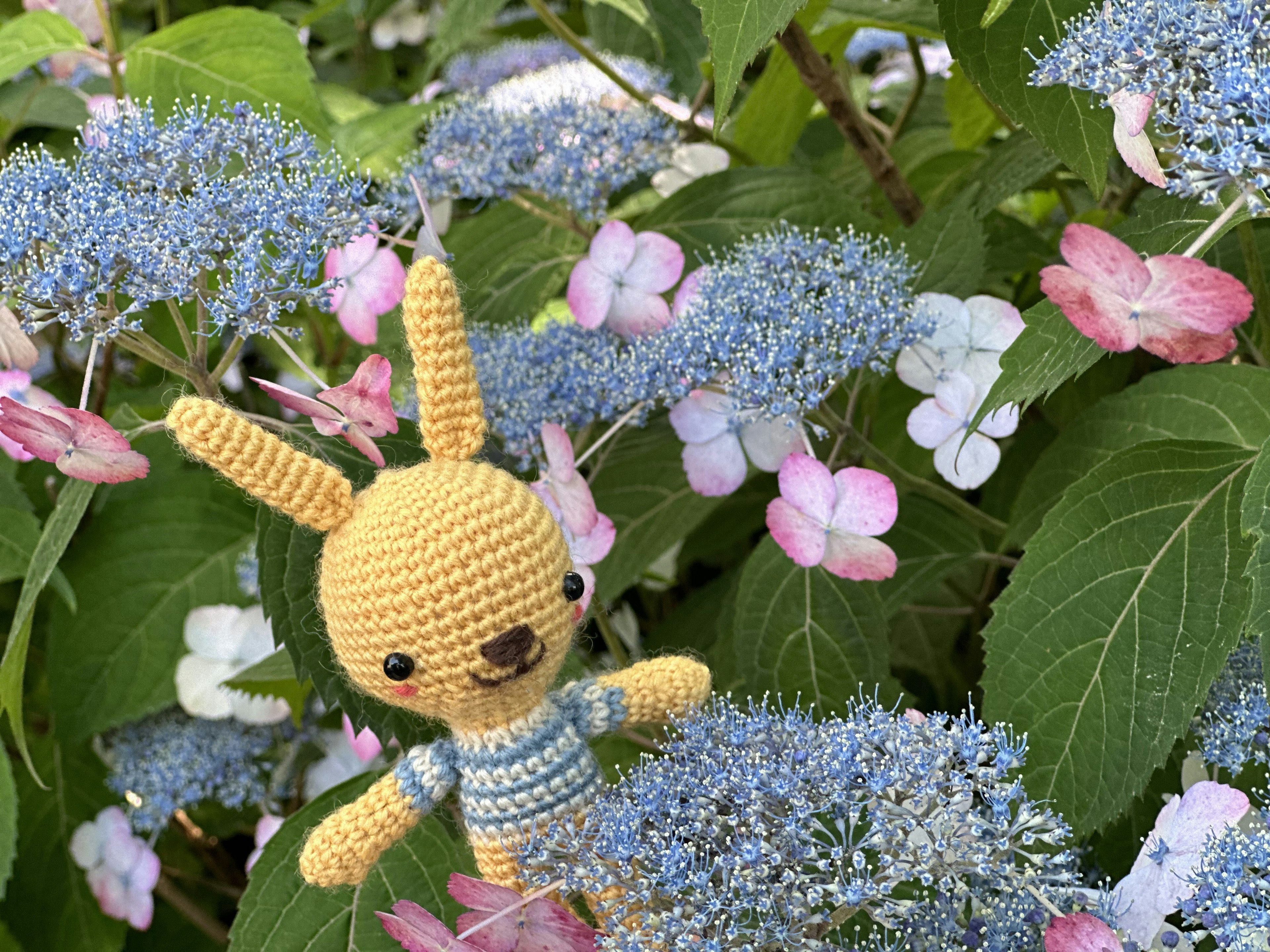 Ein gelbes Stoffkaninchen zwischen blauen und rosa Blumen