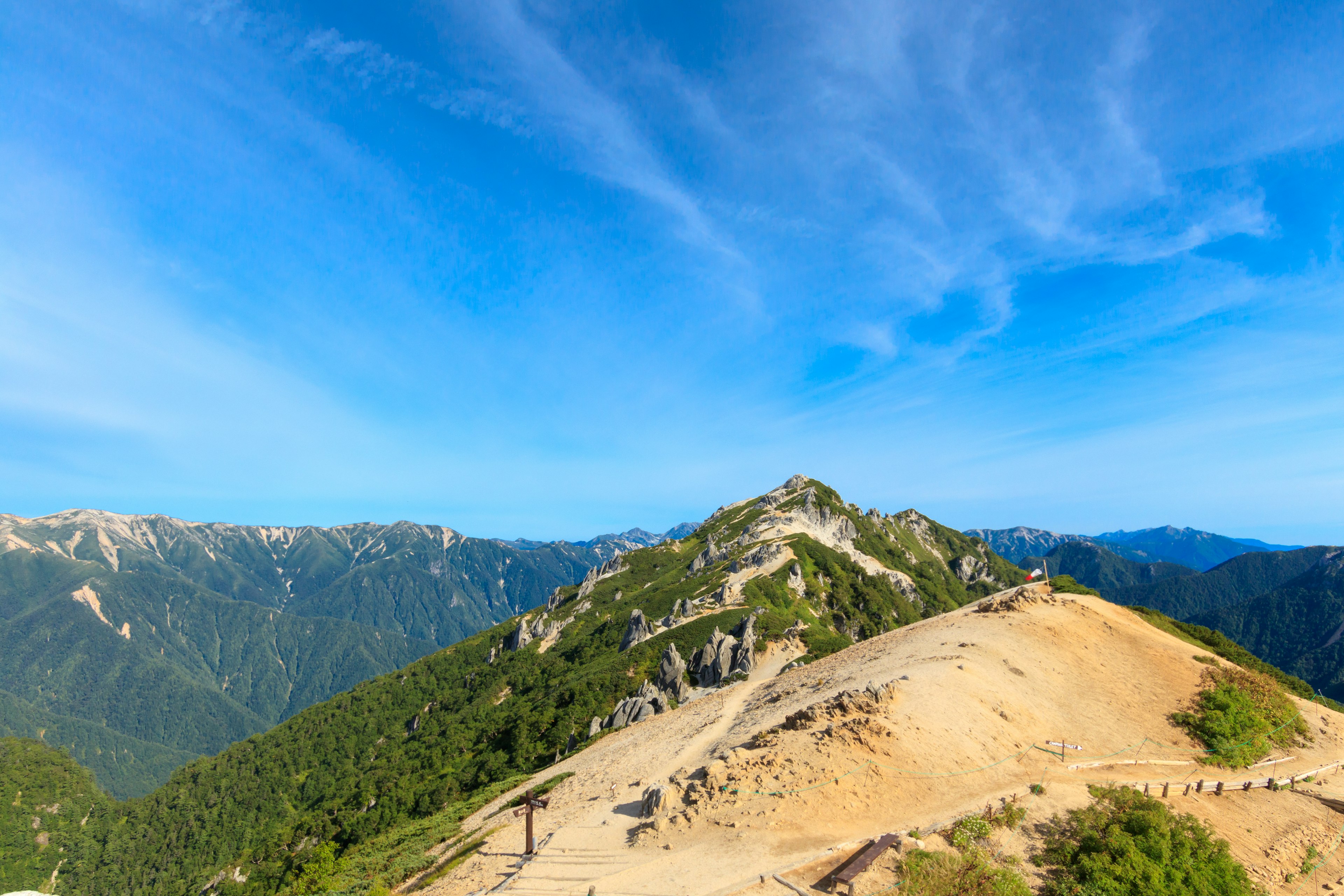 Paisaje montañoso bajo un cielo azul árboles verdes y colina rocosa visibles montañas distantes