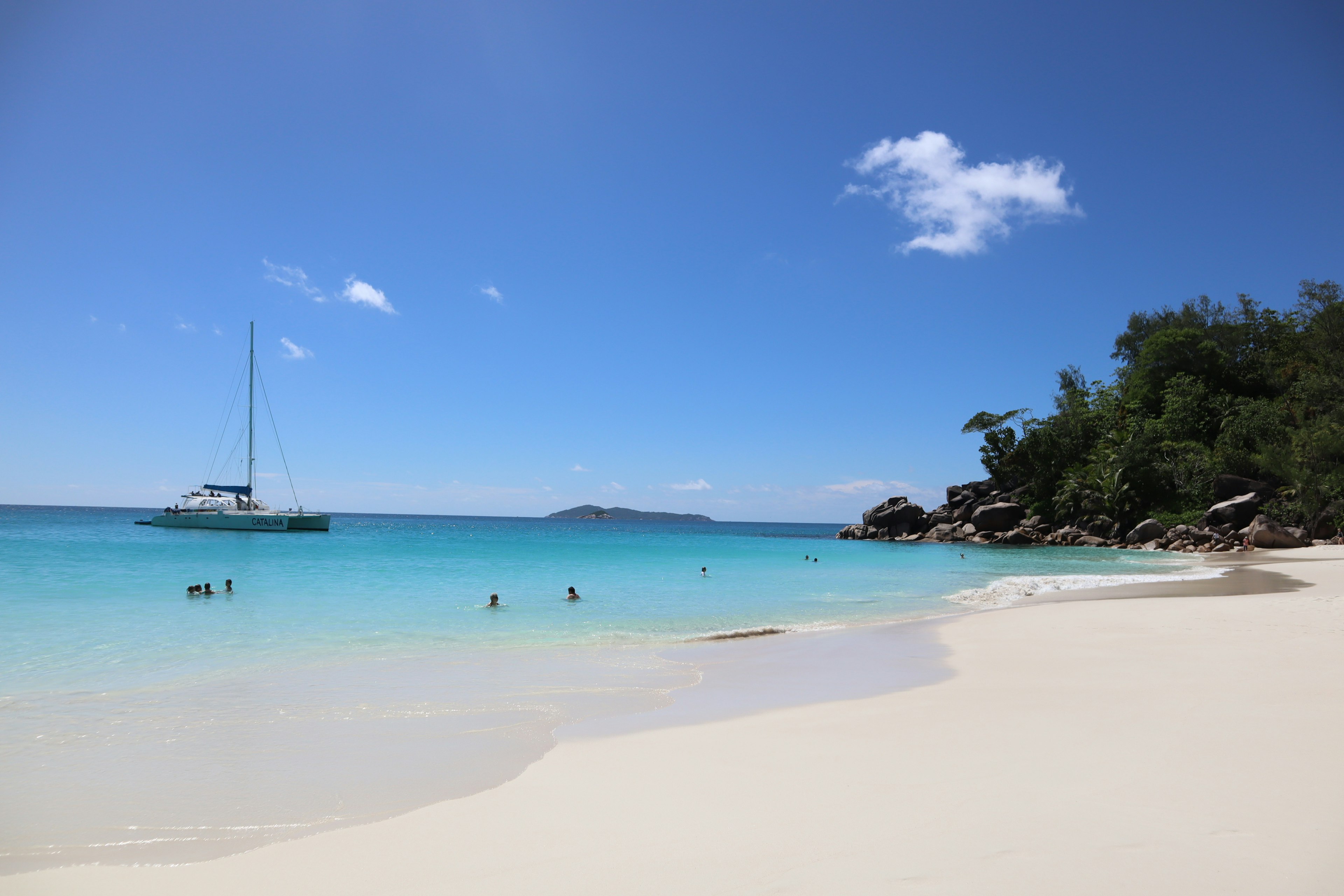 Plage magnifique avec eau turquoise bateau à voile et personnes nageant