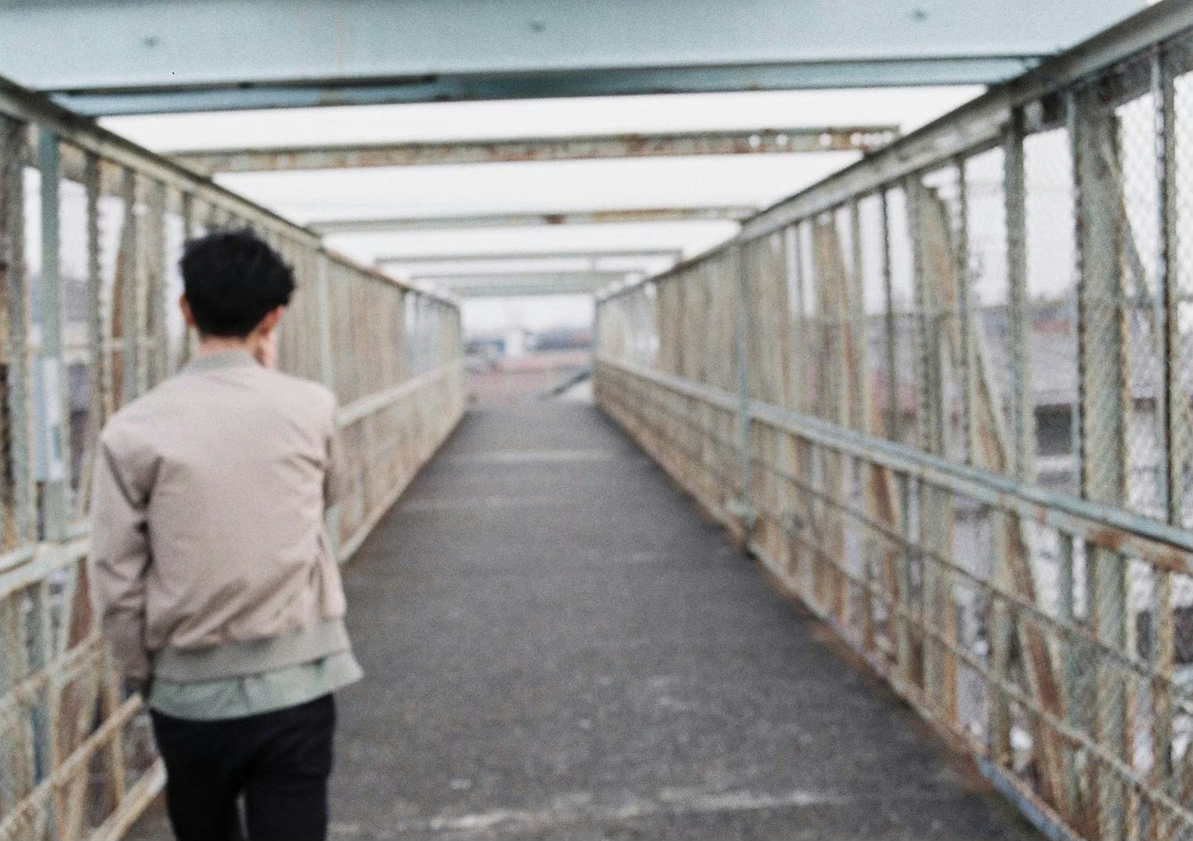 Man walking on a bridge with metal railings and concrete path