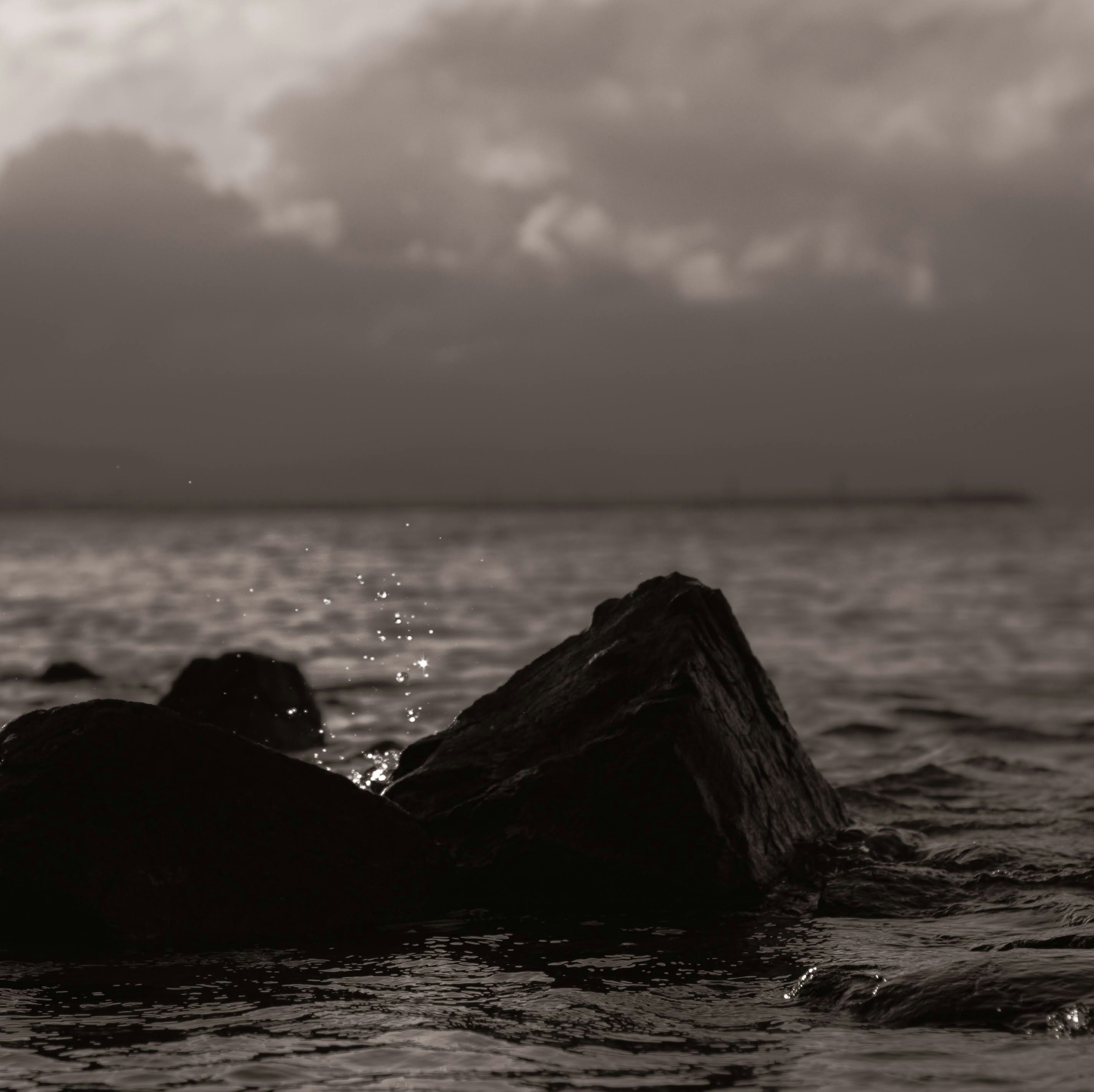 Foto hitam putih dari batu di laut dengan percikan air