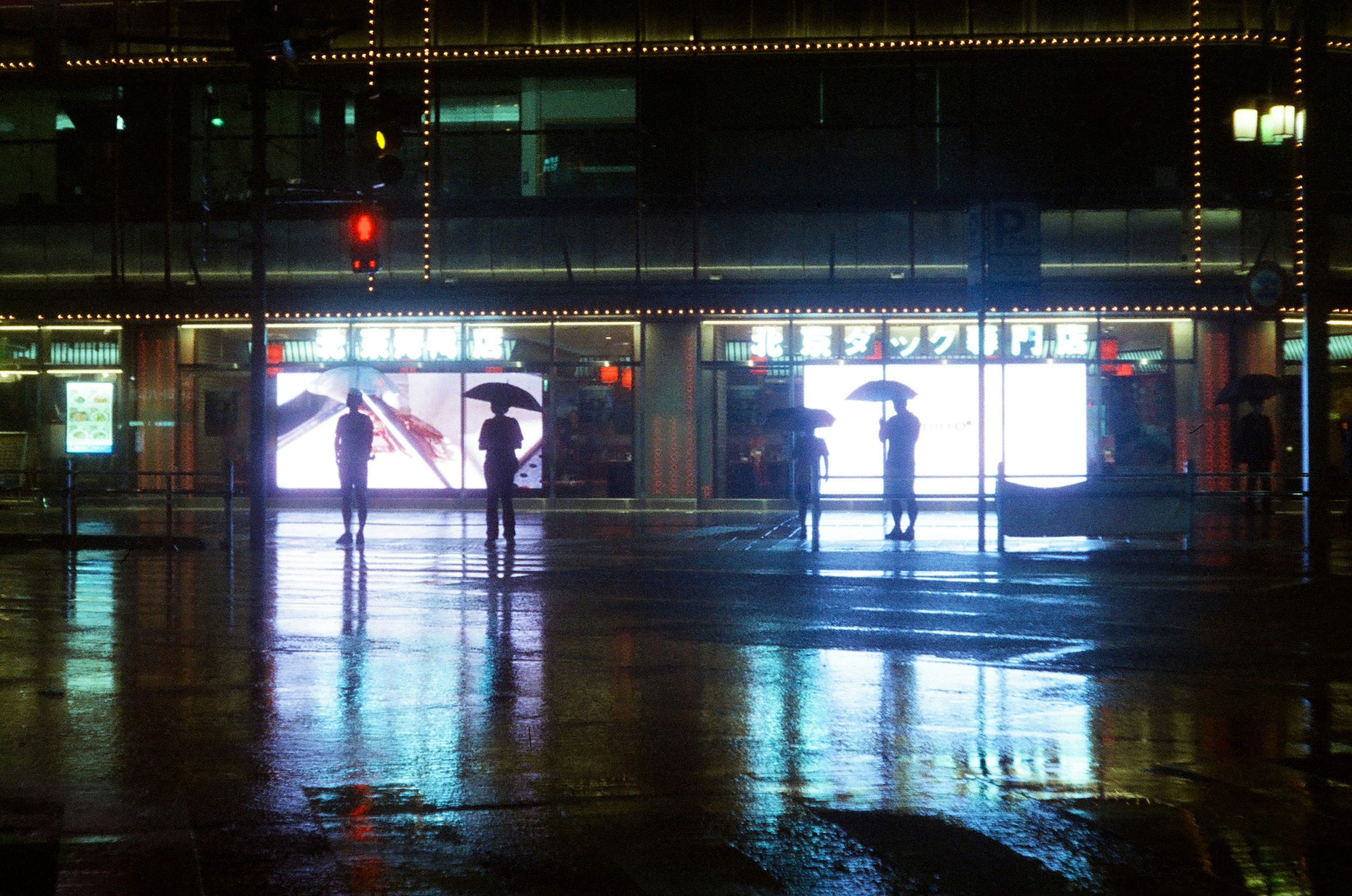 雨天街角，人們撐著傘，明亮的廣告倒影