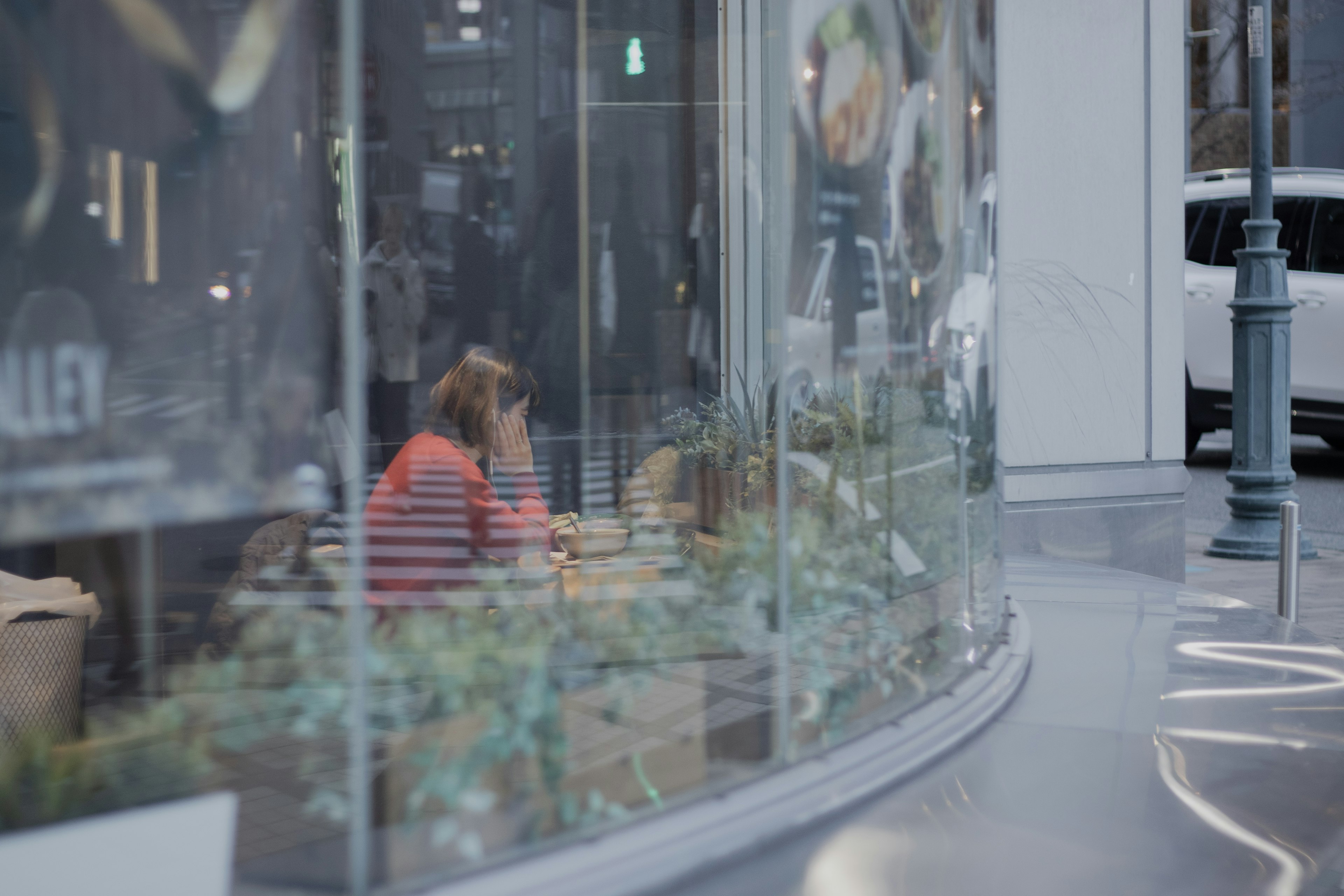 A woman deep in thought inside a café visible through glass with surrounding plants