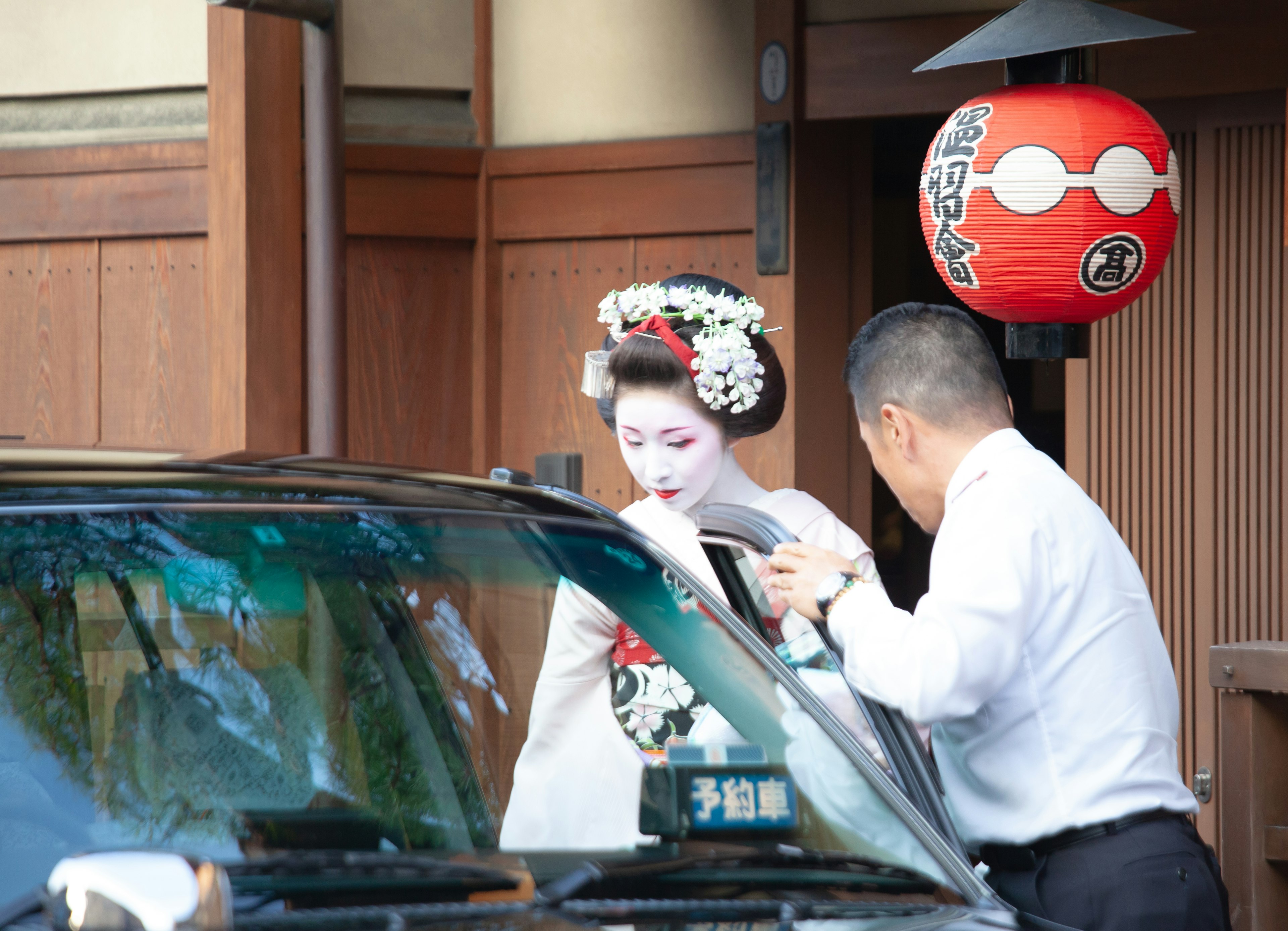 A geisha in a traditional kimono is being assisted by a man to exit a car