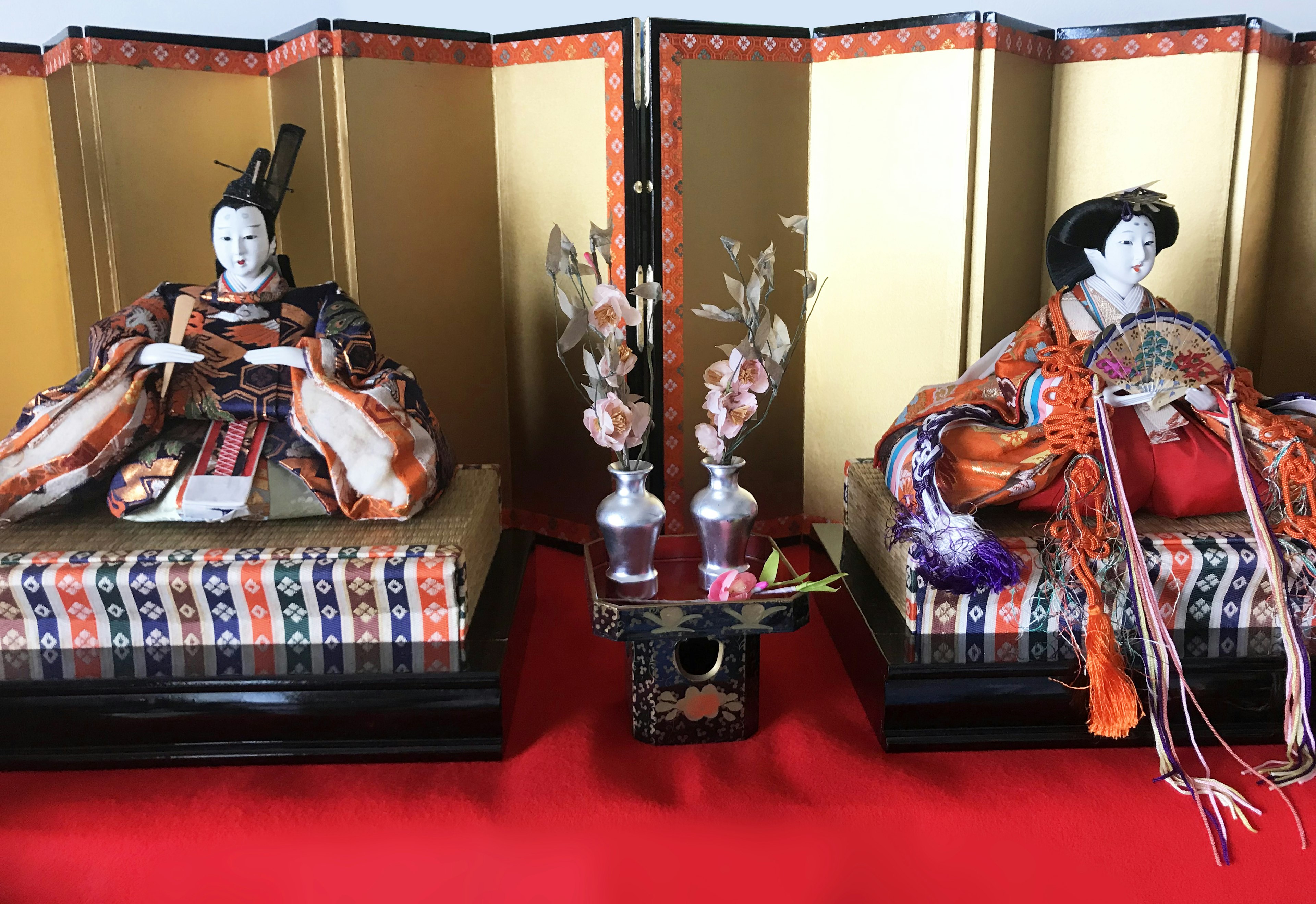 Traditionelle japanische Hina-Puppen, die mit einem dekorativen Faltbildschirm und Vasen präsentiert werden