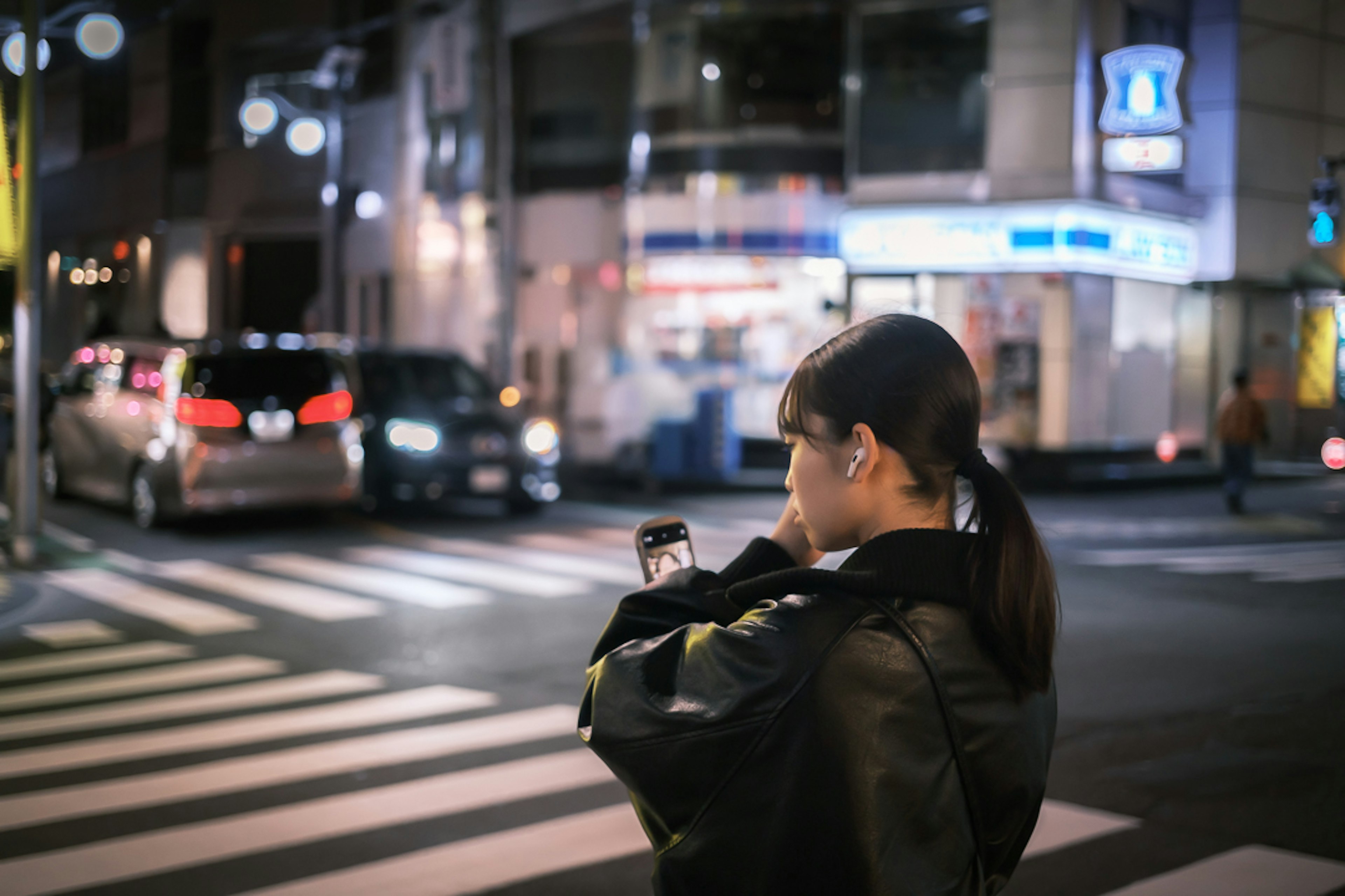 Frau, die nachts an einer städtischen Kreuzung ein Smartphone benutzt