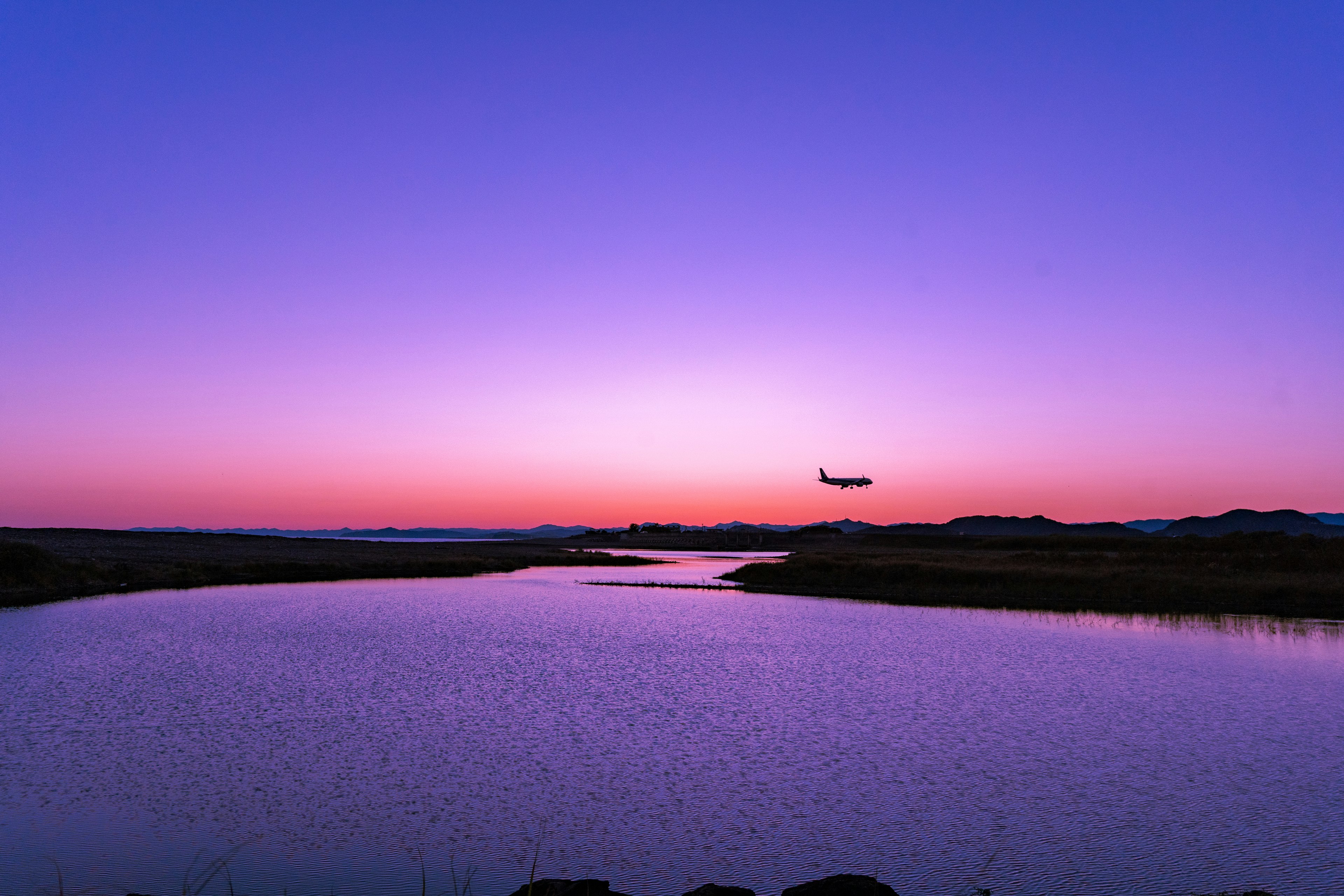 夕暮れの空に浮かぶ飛行機と静かな川の風景