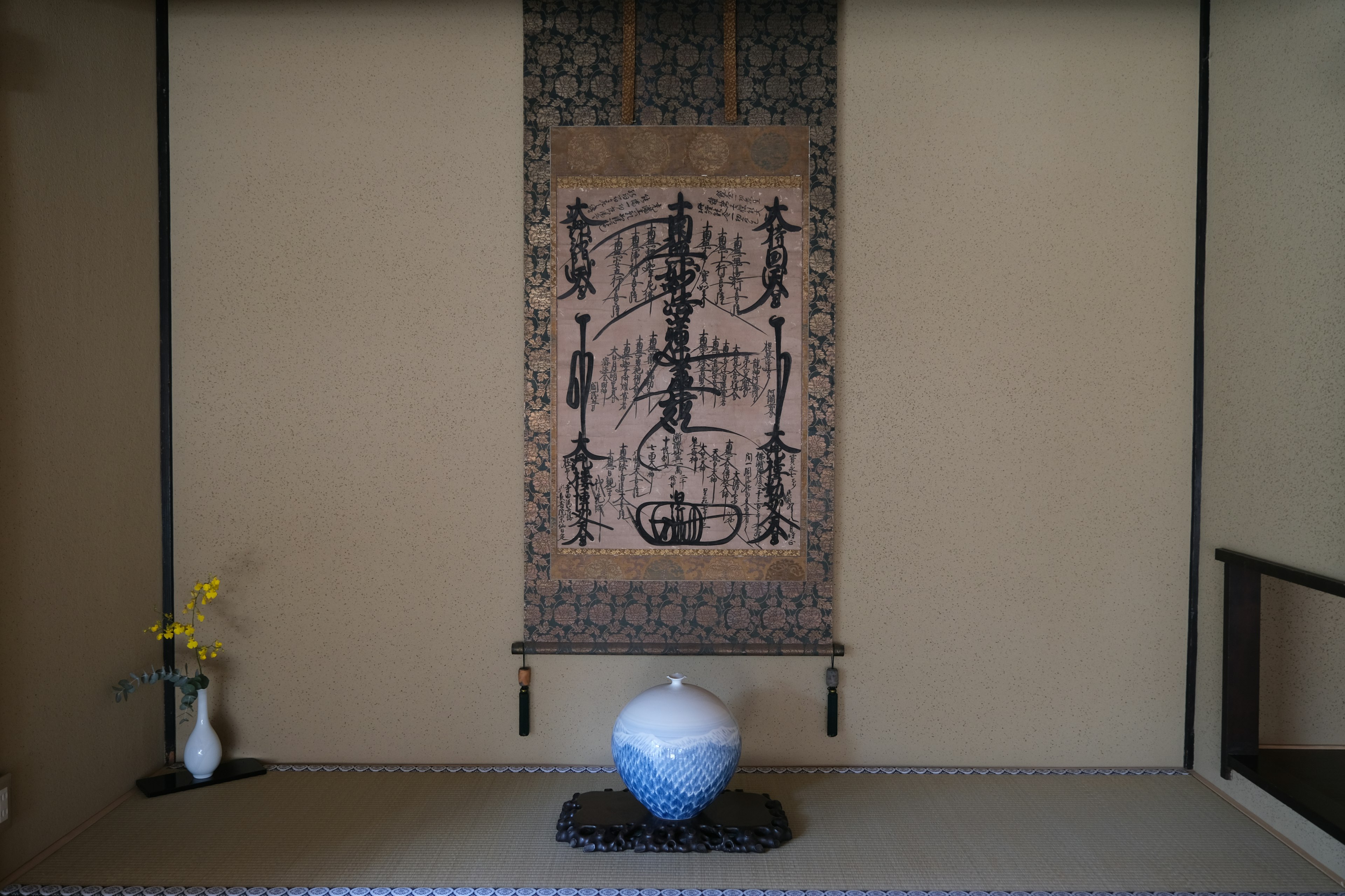 Habitación japonesa tradicional con un rollo de pintura en tinta colgado y un jarrón azul en una estantería