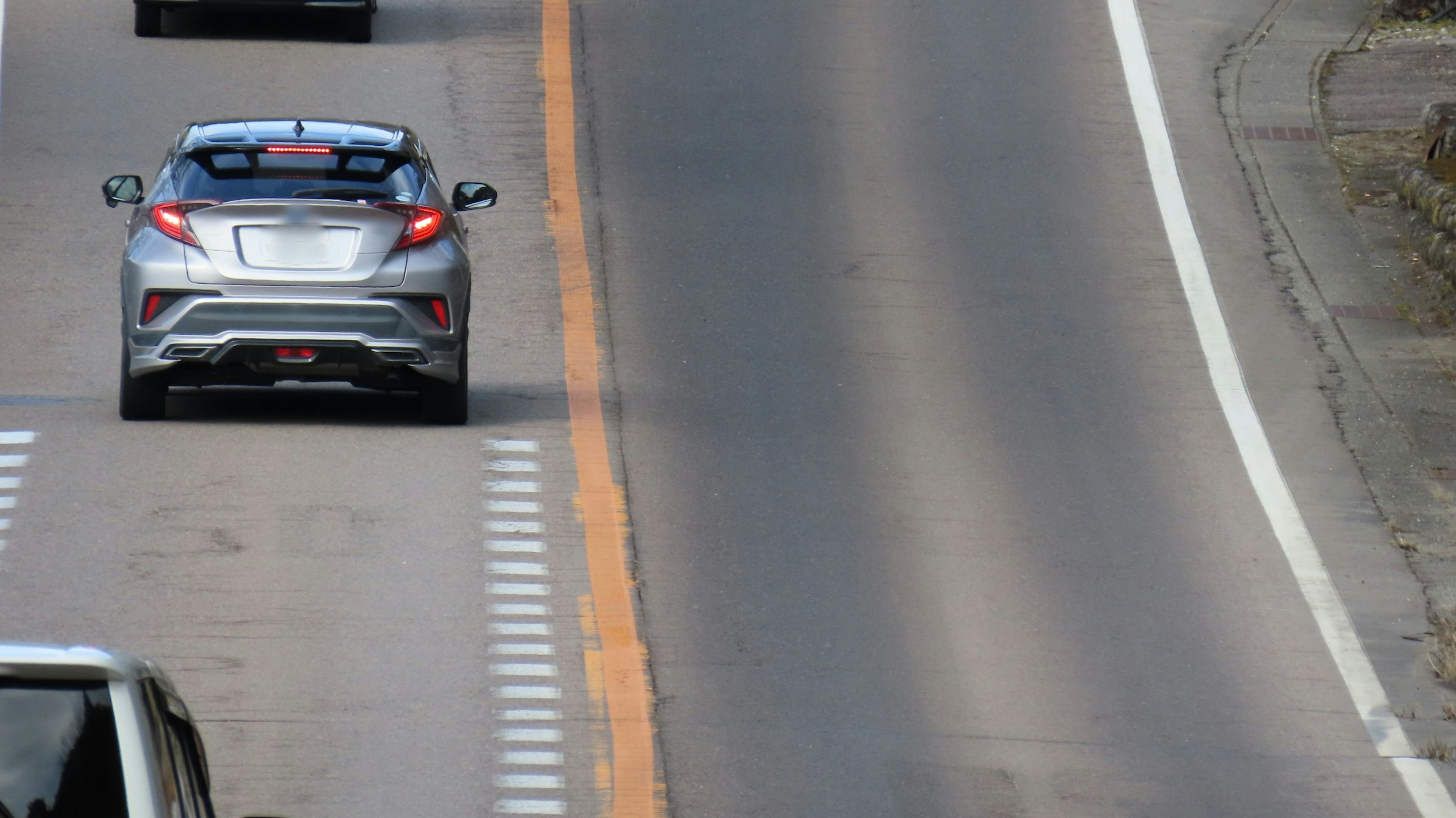 Mobil perak melaju di jalan raya dengan tanda jalur oranye