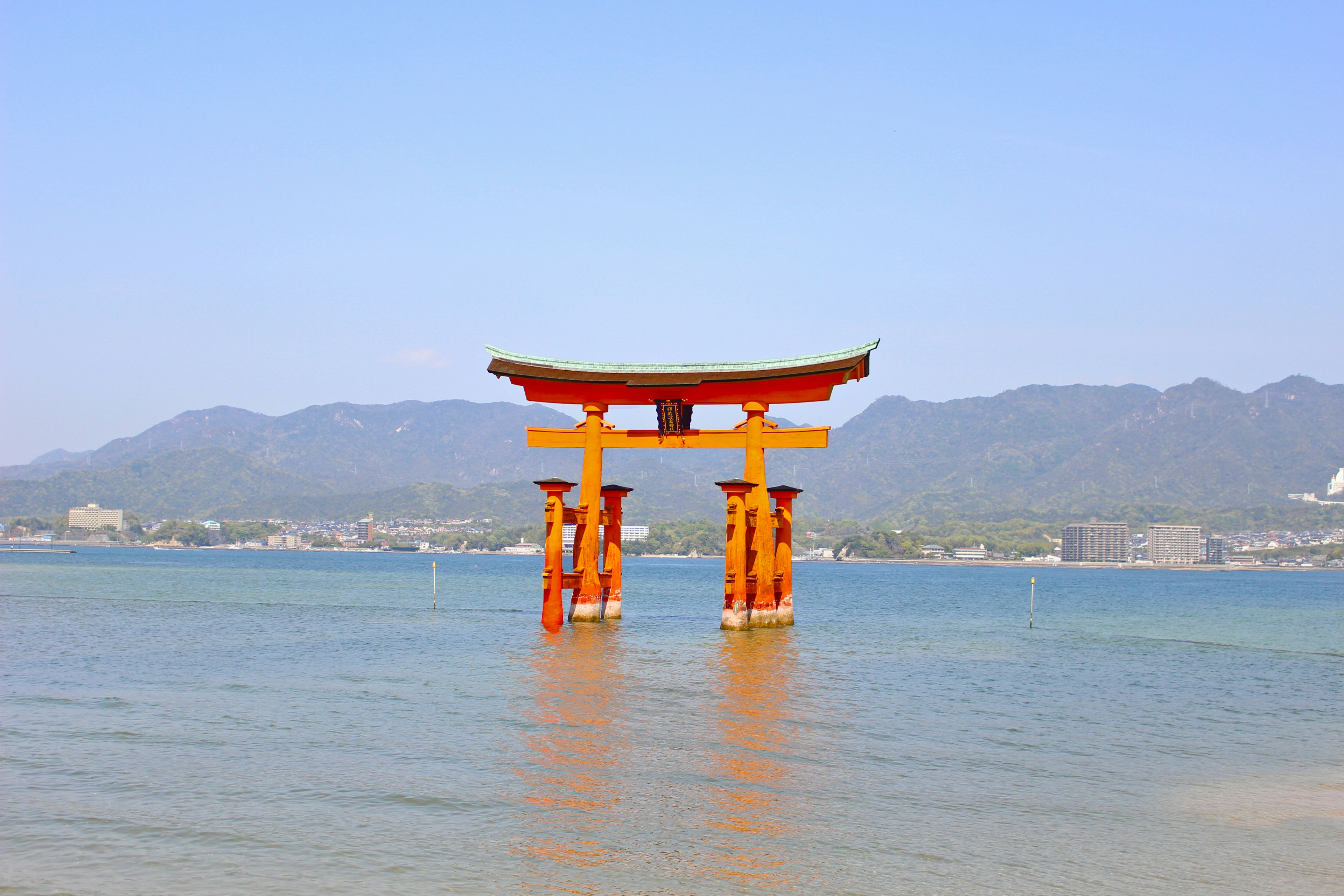 Red torii gate standing in shallow water with mountains in the background