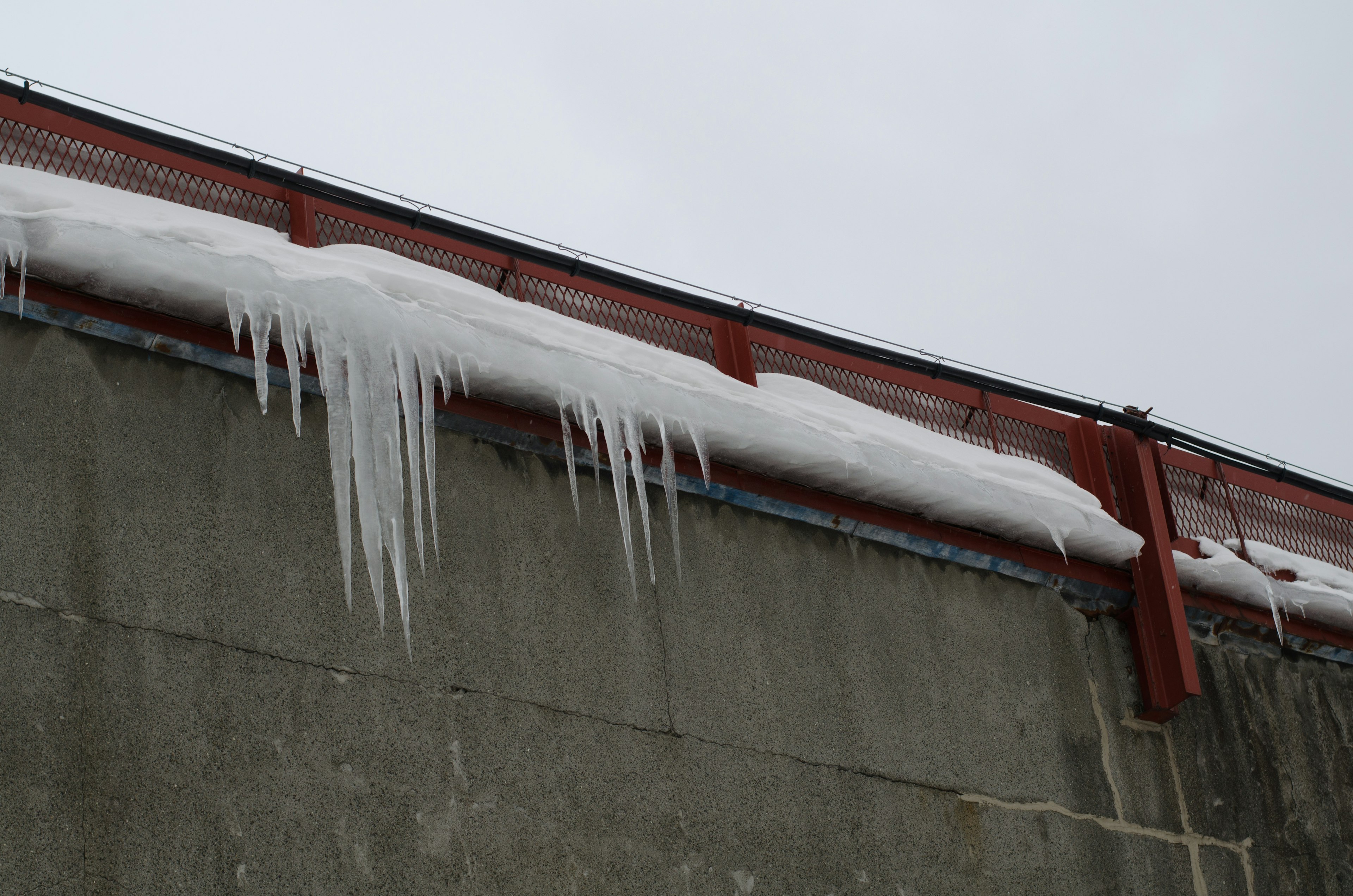 屋根の雪と氷柱のあるコンクリート壁の画像