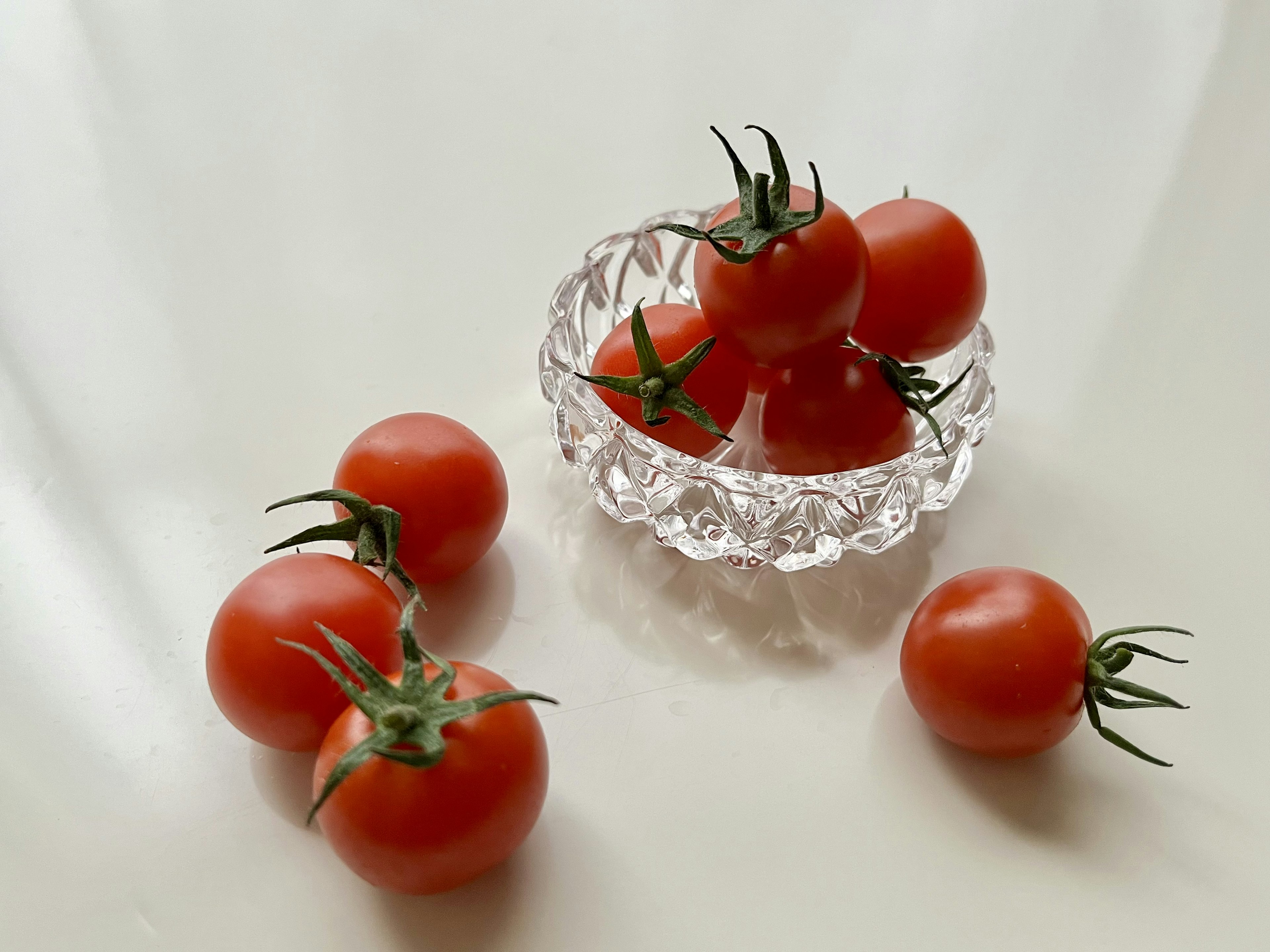 Pomodori freschi disposti in una ciotola di cristallo con pomodori aggiuntivi sparsi attorno