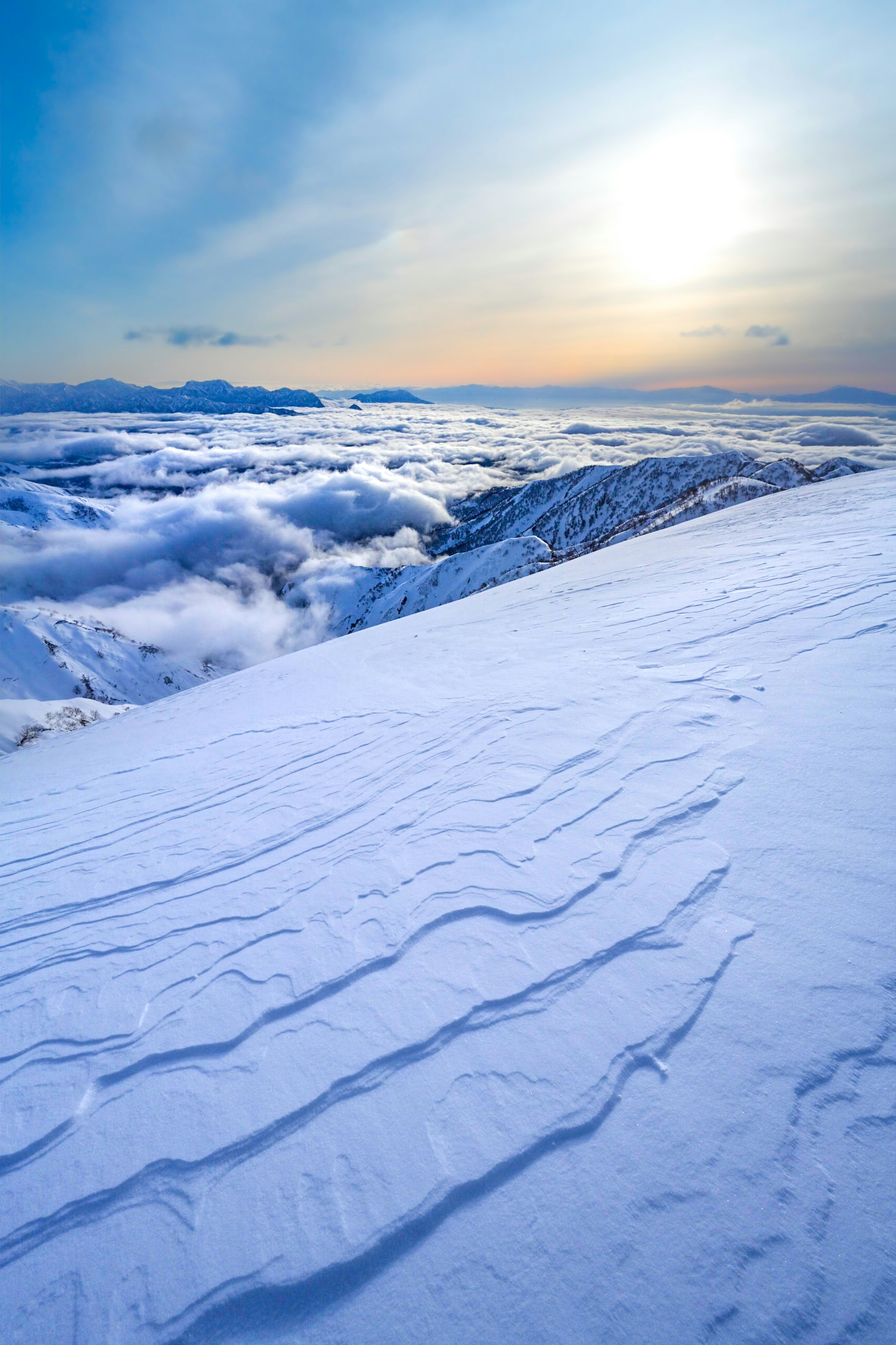 Ladera de montaña cubierta de nieve con un mar de nubes y un atardecer