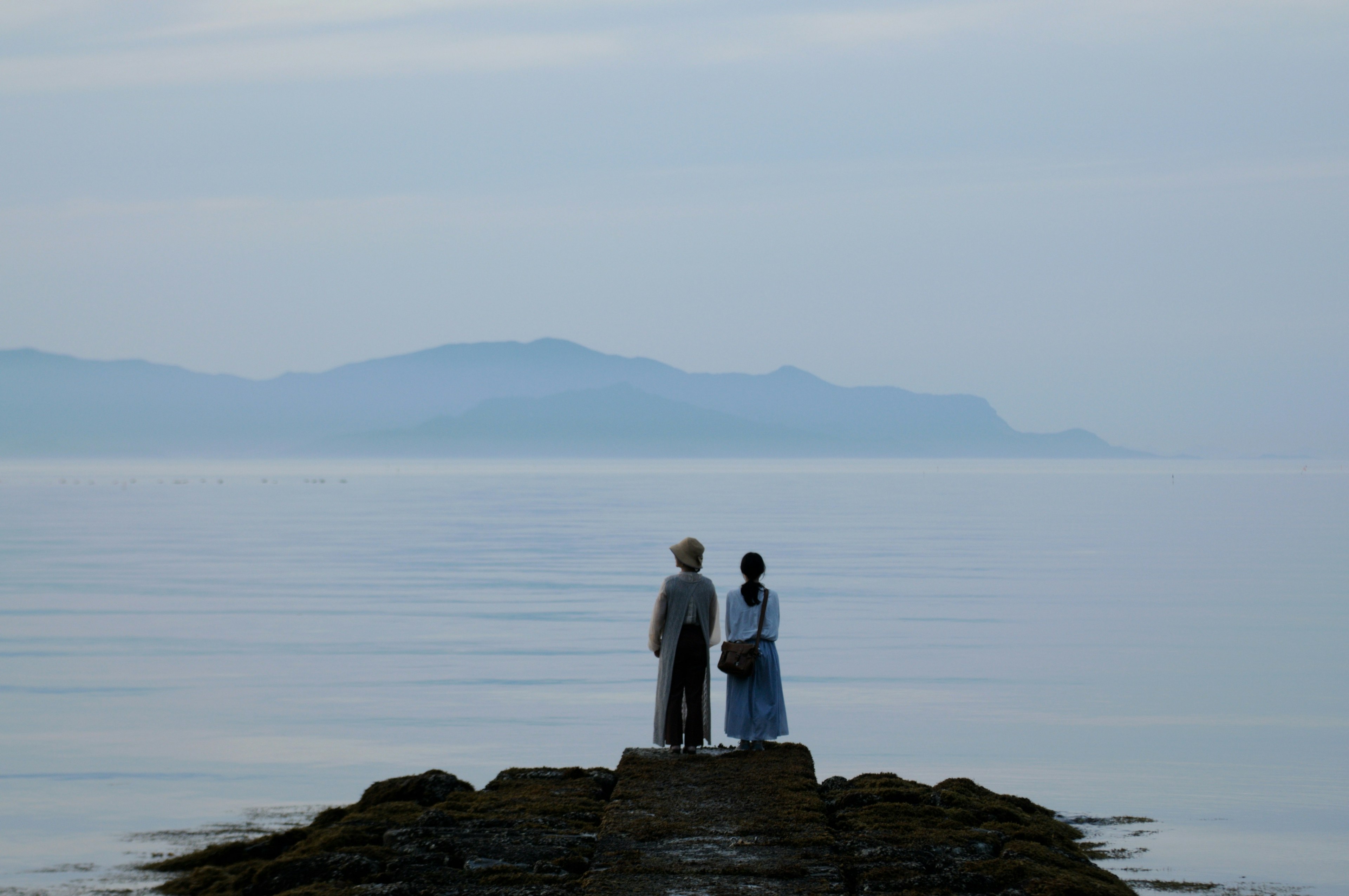 静かな海の上に立つ二人の人物が写っている