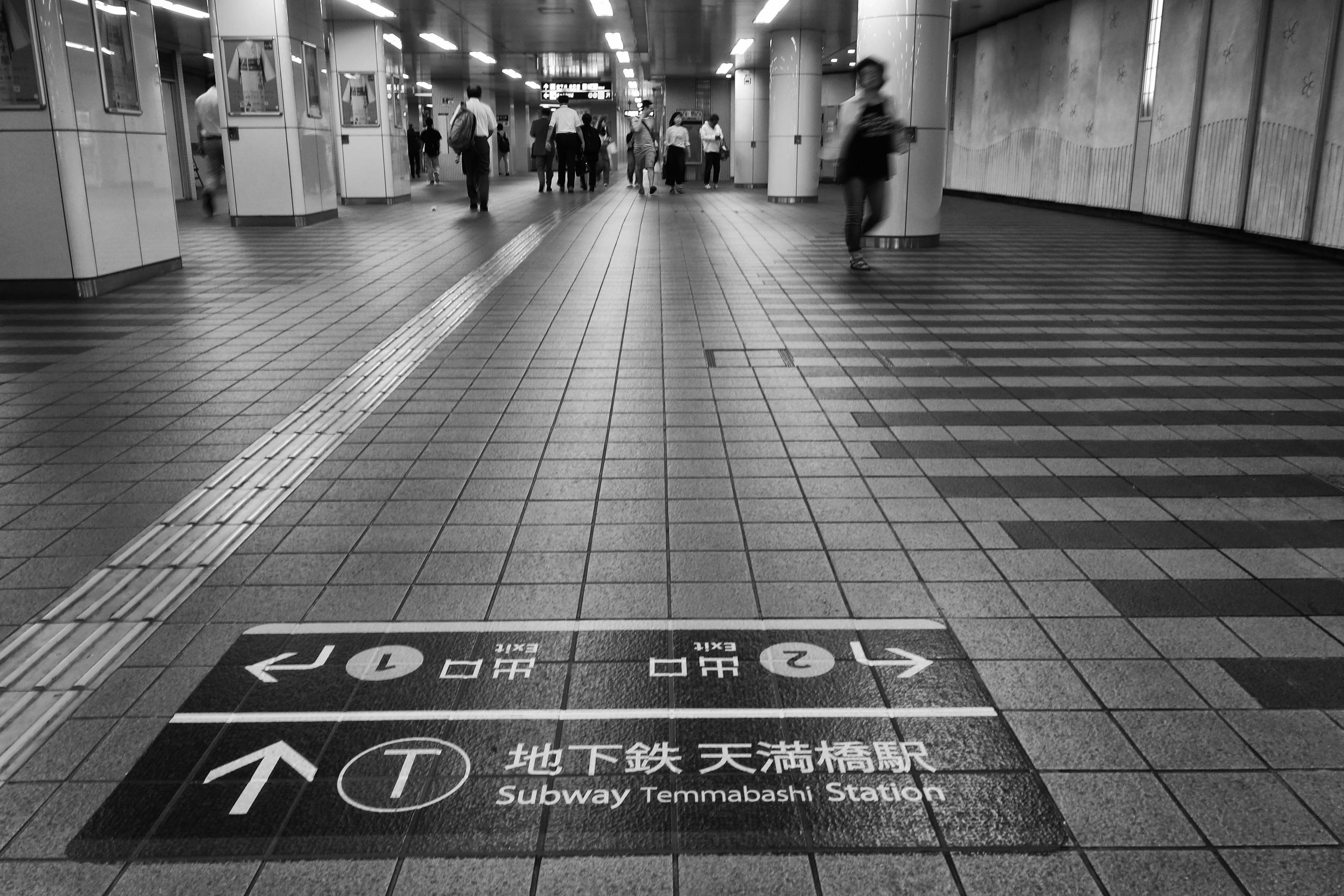 Signalisation au sol indiquant la station de métro Tenman avec des flèches directionnelles