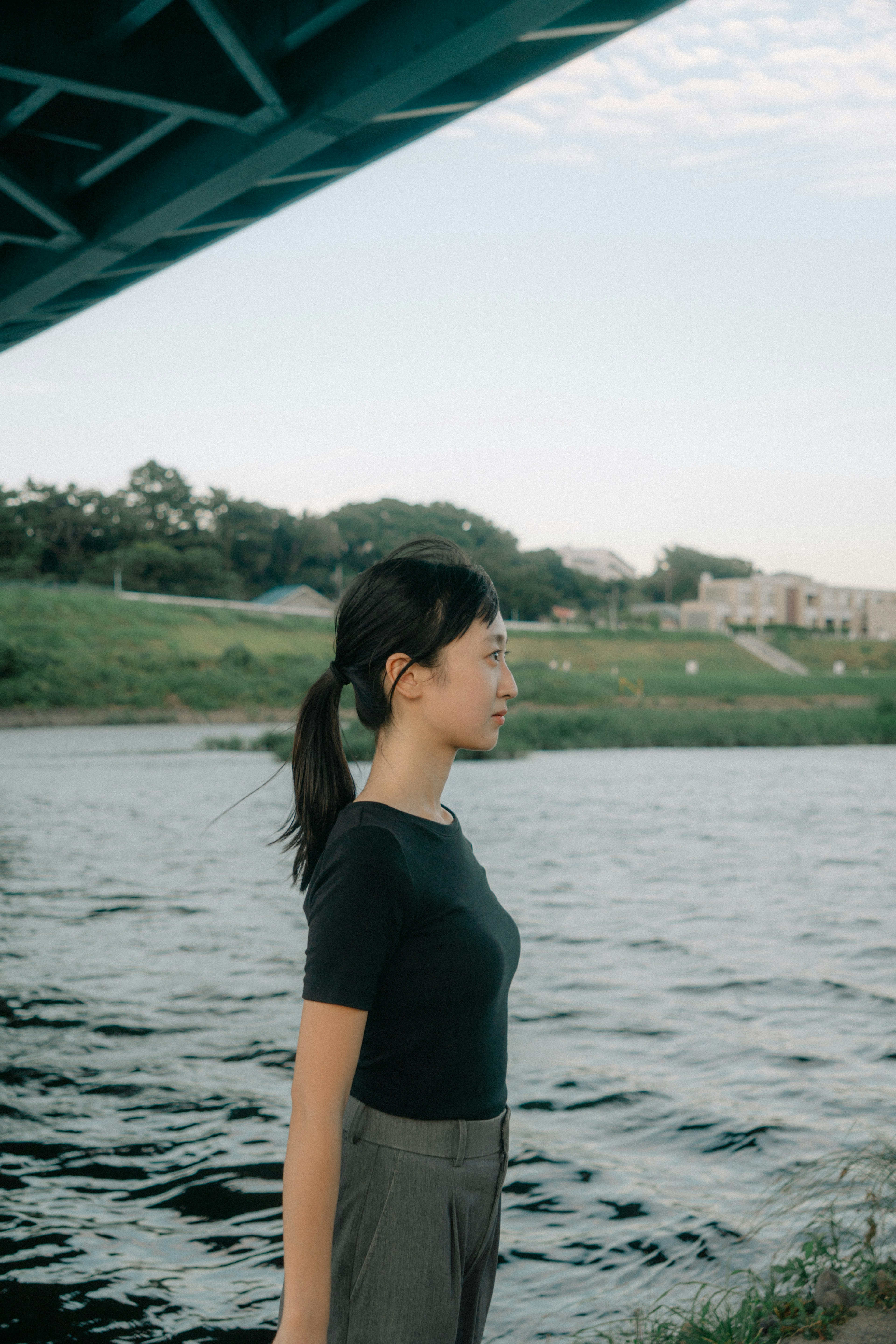 Profil d'une femme debout au bord d'une rivière avec de l'herbe verte et de l'eau en arrière-plan