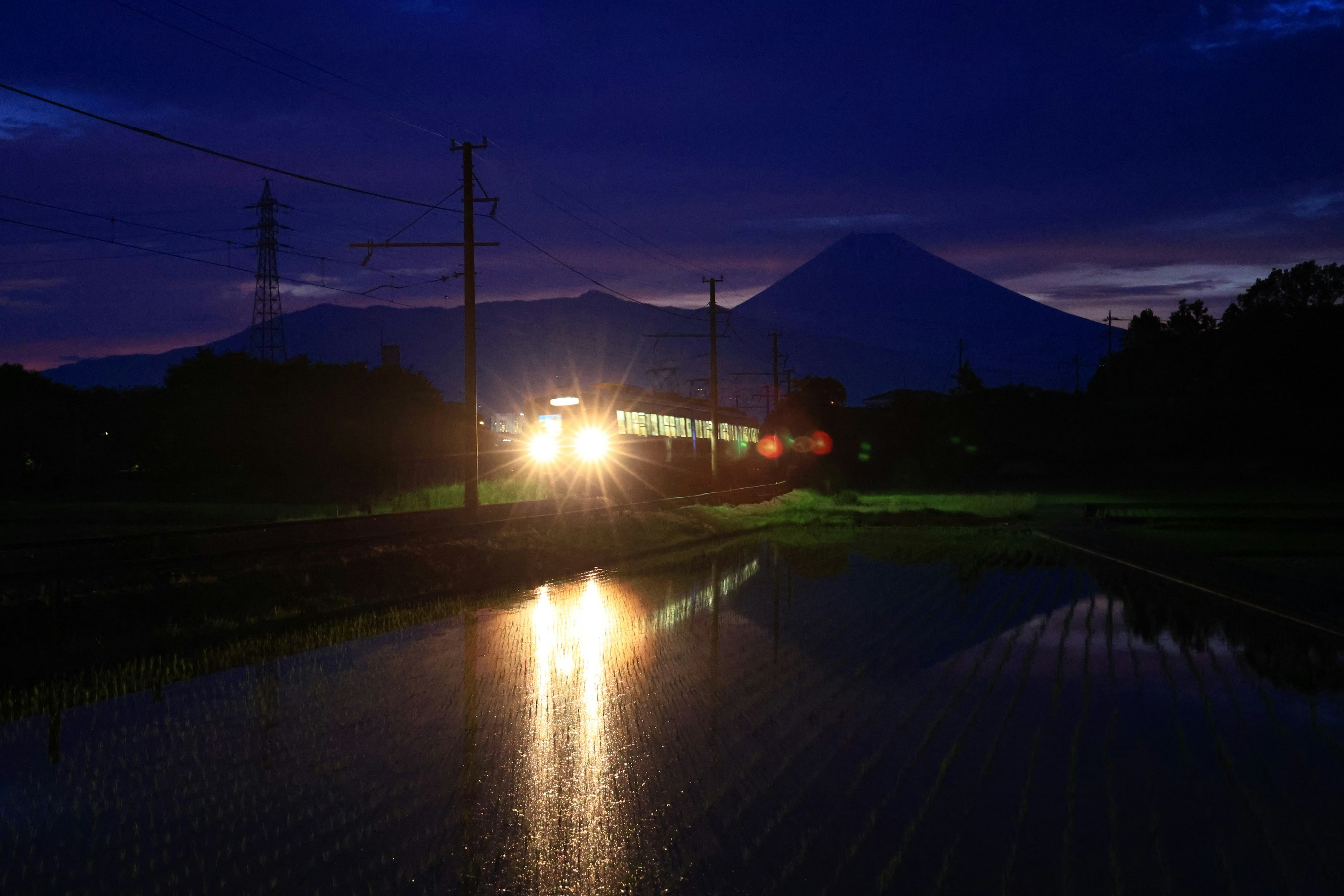 Luci del treno che illuminano il paesaggio al crepuscolo con montagne e risaie